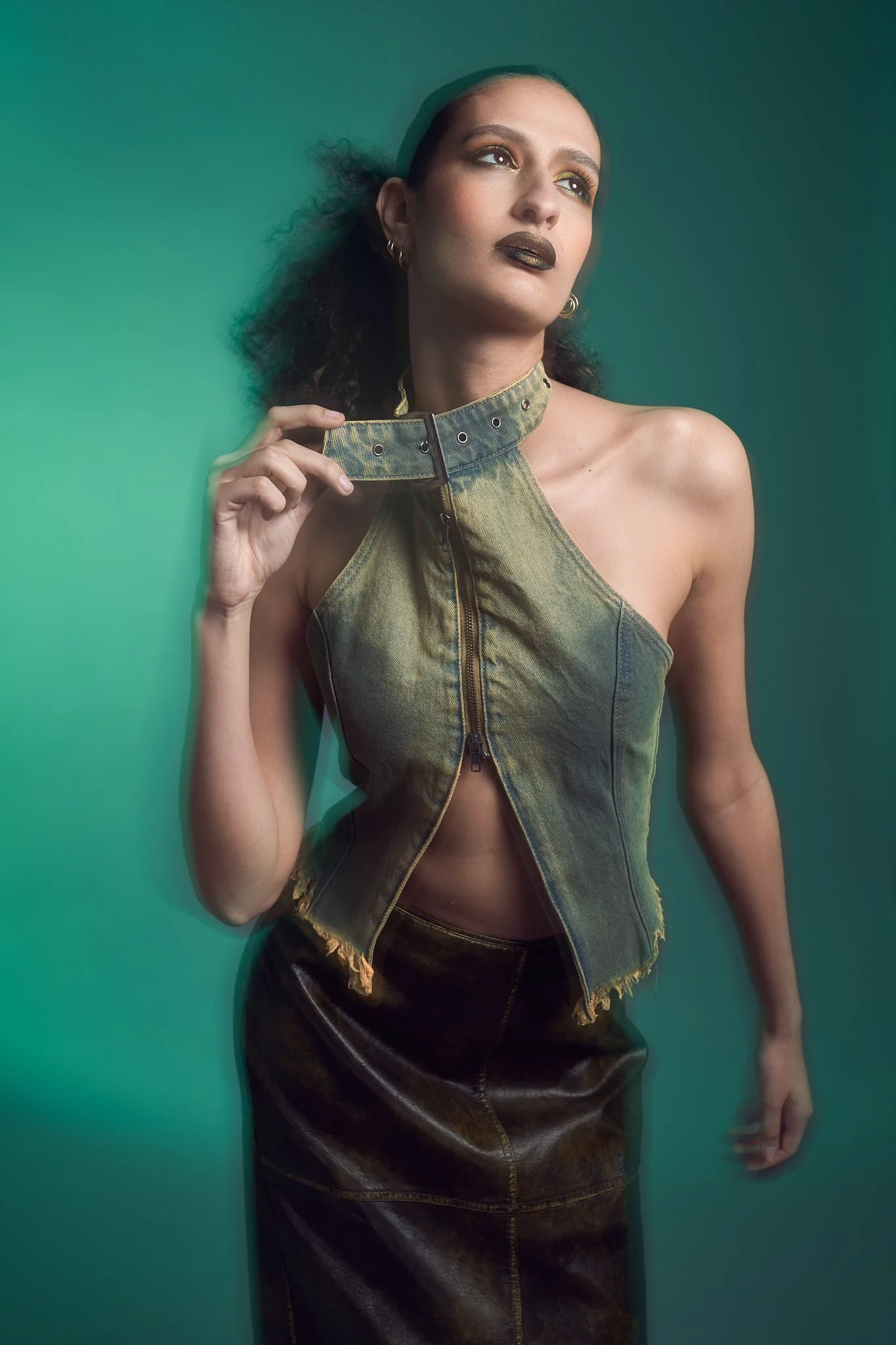 Atmospheric studio fashion portrait of a model in a deconstructed Jaded London denim halter top and leather skirt, shot against a hazy emerald green backdrop with painterly light.