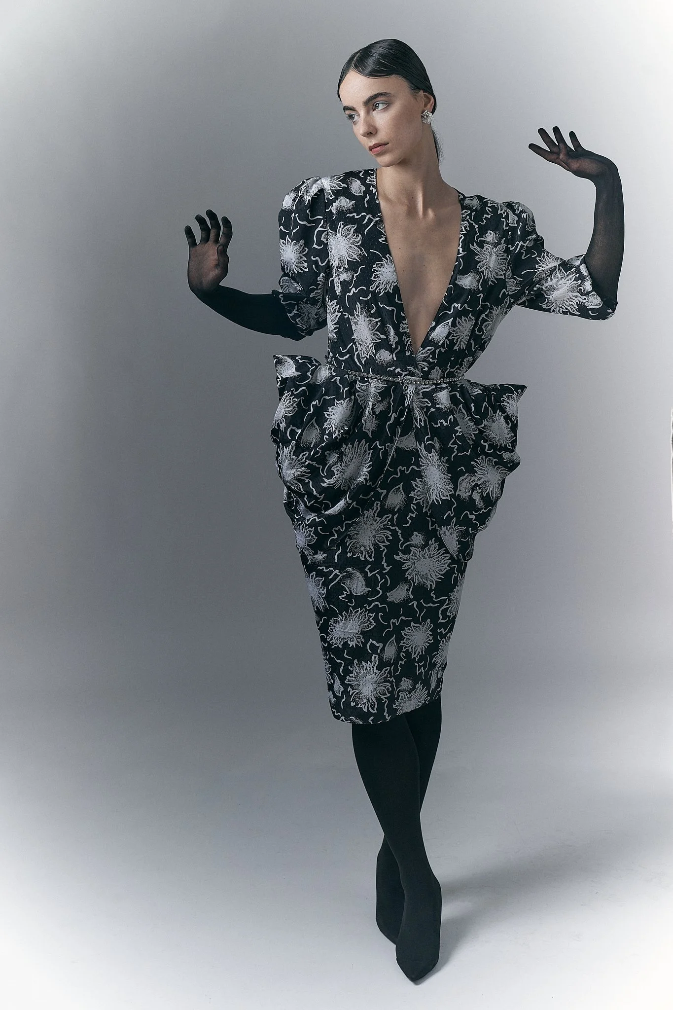 ⁠Full-length fashion portrait of a model in a black-and-white patterned dress with structured hip hip detailing and black sheer gloves.⁠