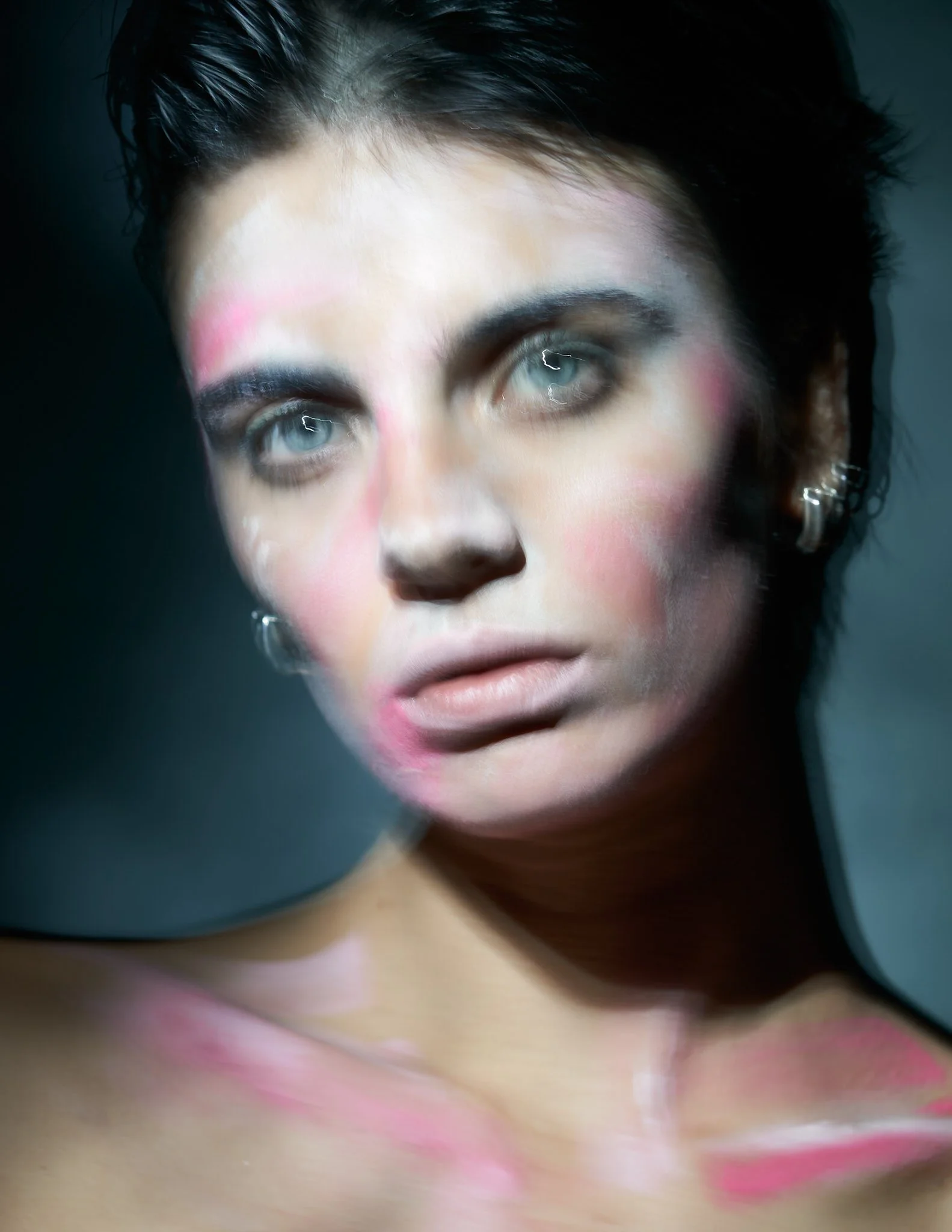 Close-up beauty editorial portrait featuring a dark-haired model with high-concept pink pigment makeup brushed across the cheeks, nose, and collarbones.⁠