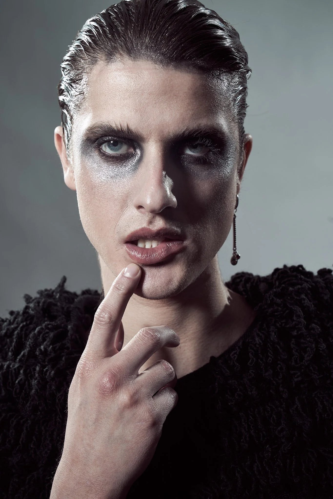 Tight close-up editorial portrait of a male model featuring intense dark smoky eye makeup, slicked hair, and a subtle drop earring.⁠