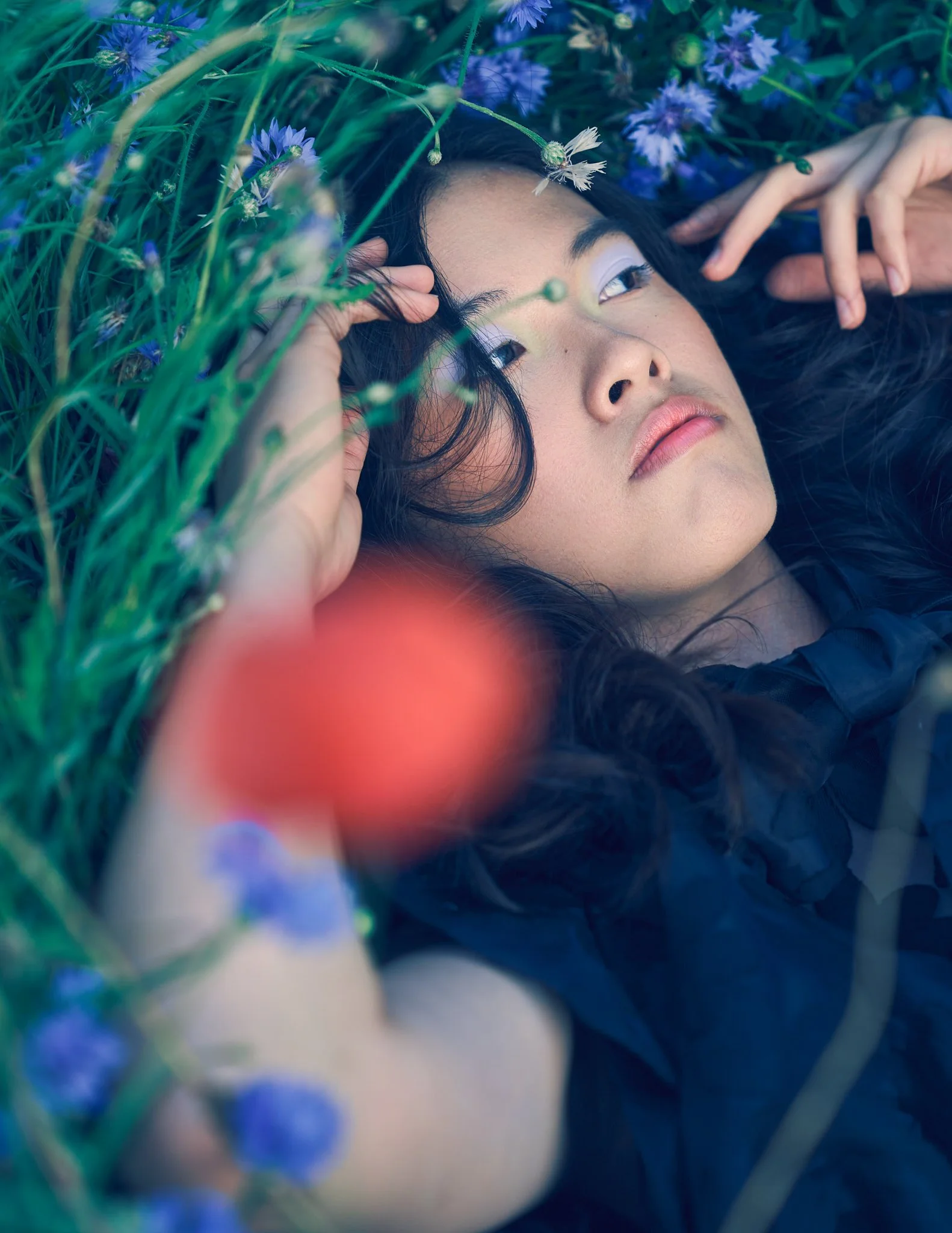 Dreamlike fine art portrait of a woman lying in wildflowers, photographed in Belgium in an editorial, fashion-inspired style.