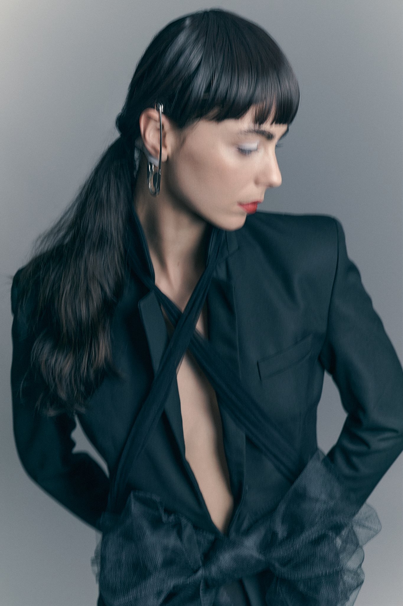 Profile portrait of a brunette model with dark bangs wearing a tailored dark blazer against a minimal studio background.⁠
