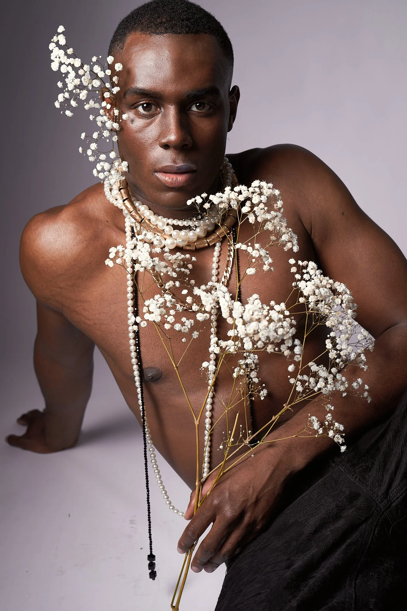 A shirtless male model adorned with pearl necklaces and gypsophila blossoms gazes directly at camera, studio fashion portrait by Simon Rogghe, Animodels series.