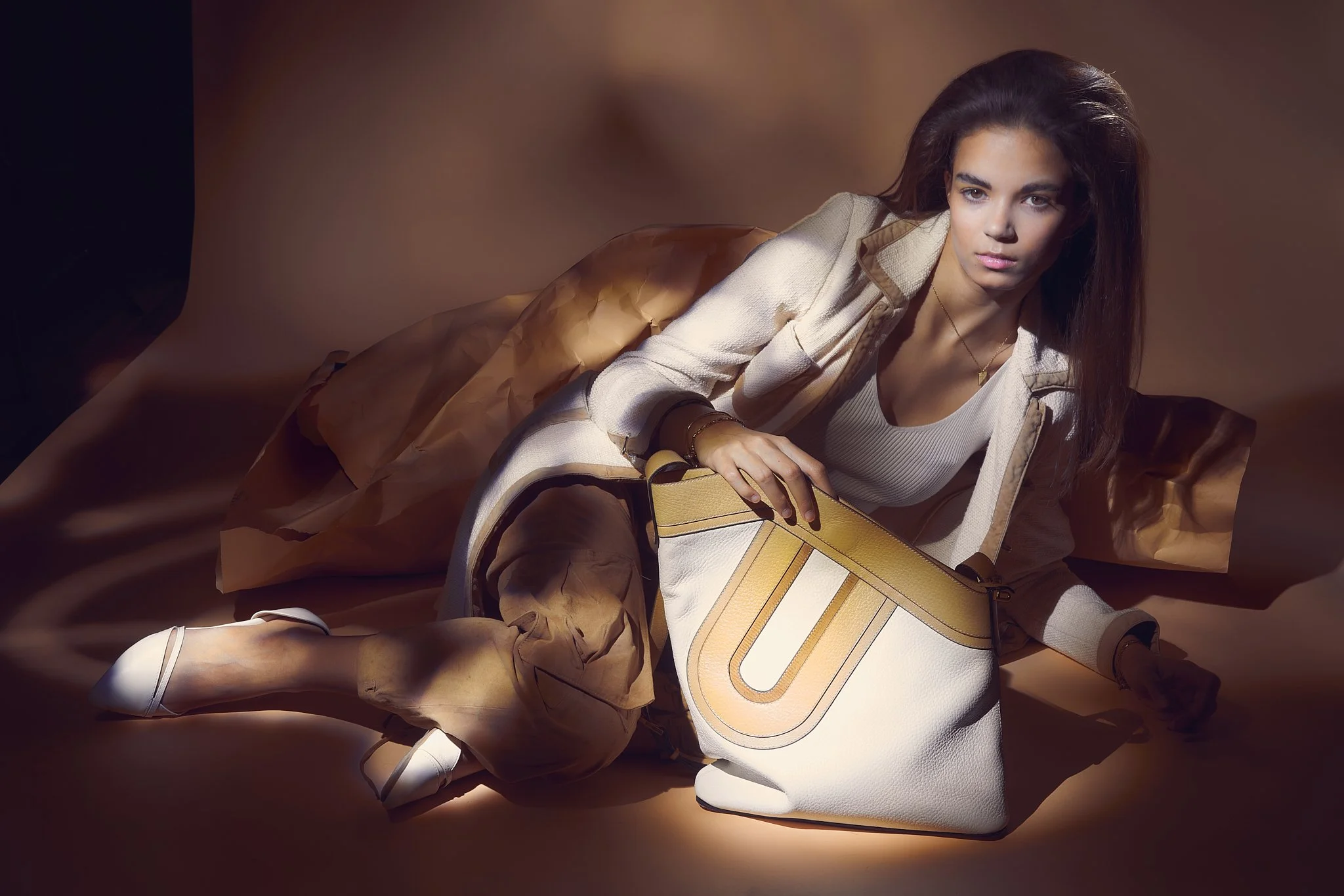 Luxury leather shoulder bag campaign with reclining model, painted with light against a warm studio backdrop — premium commercial photography by Ghent-based fashion photographer Simon Rogghe.