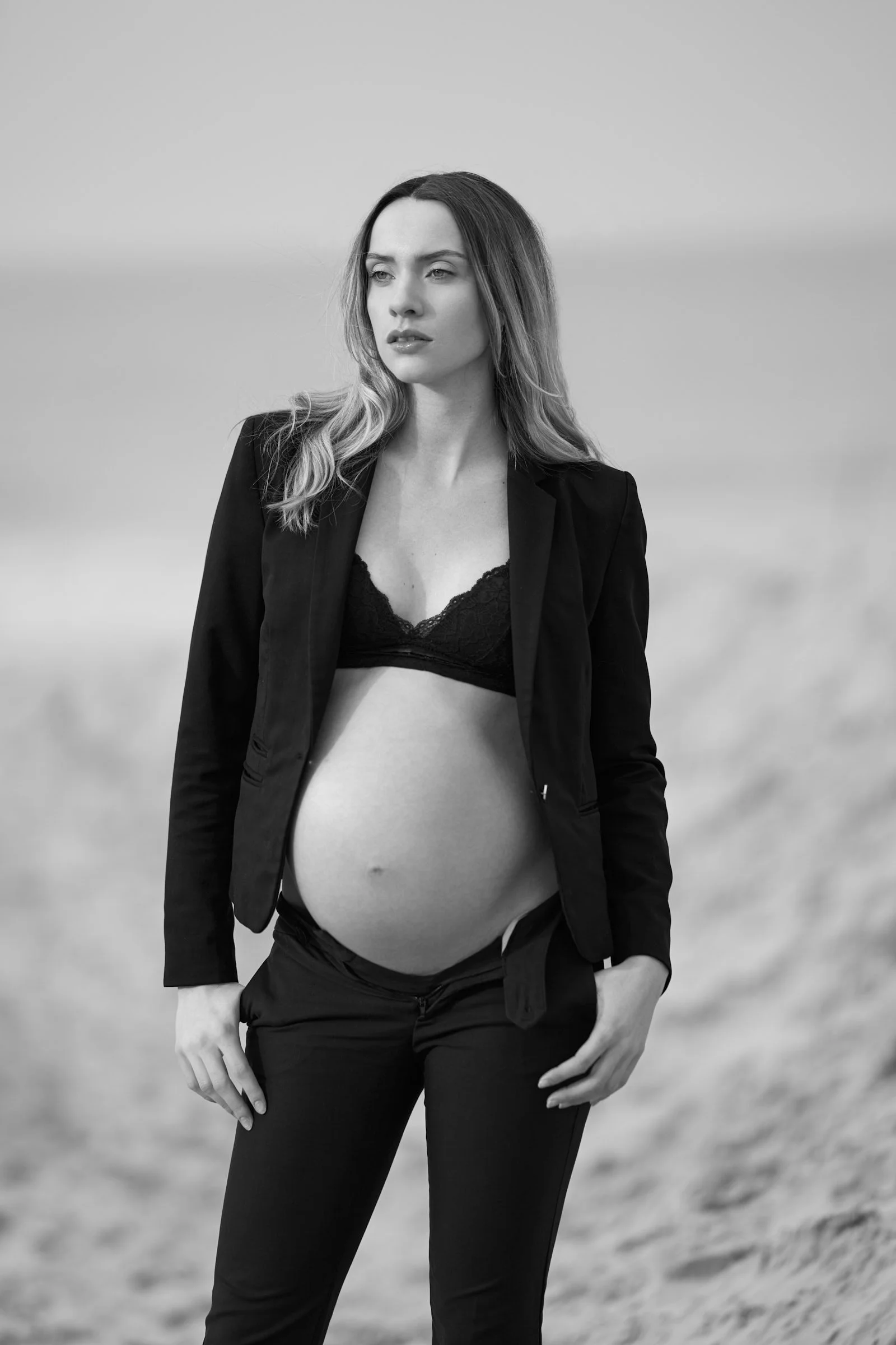 Zwart-wit zwangerschapsfoto op het strand met stijlvolle blazer – modegerichte zwangerschapsshoot aan zee in Oost-Vlaanderen.