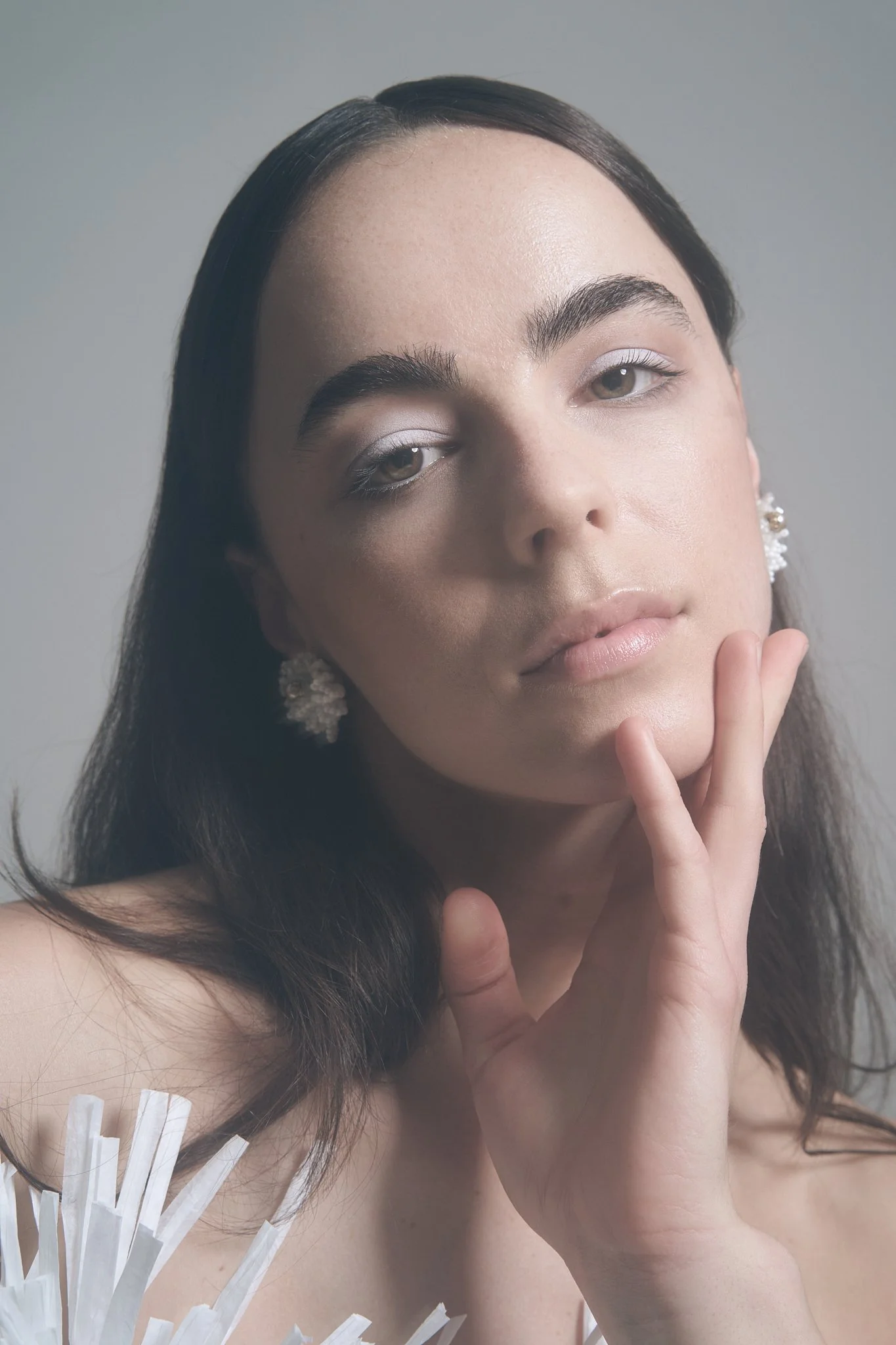 Beauty portrait of a brunette model with sleek hair and subtle metallic eye makeup, gently resting her hand near her face.⁠