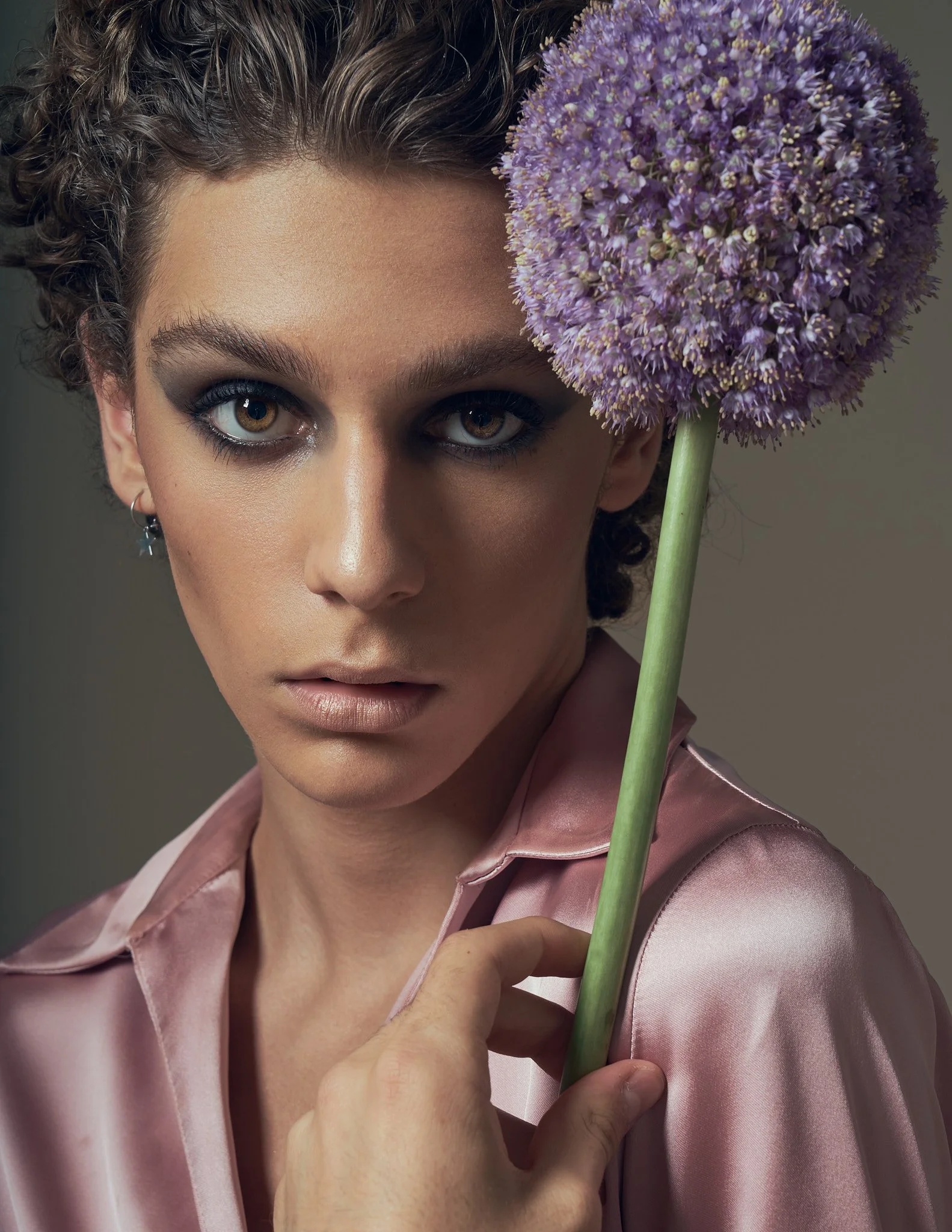 Androgynous beauty portrait with a model holding a large purple allium flower. Silky textures and subtle gender fluidity define this editorial by Flemish photographer Simon Rogghe.