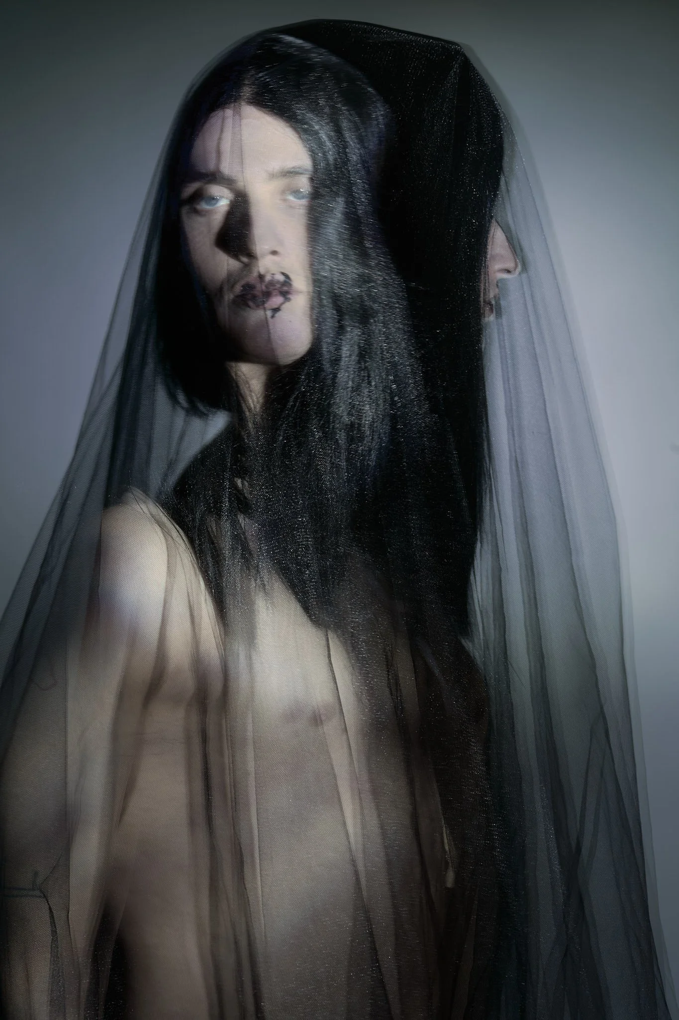 Surreal high-fashion editorial portrait of a male model draped under a delicate black sheer veil with moody lighting.⁠