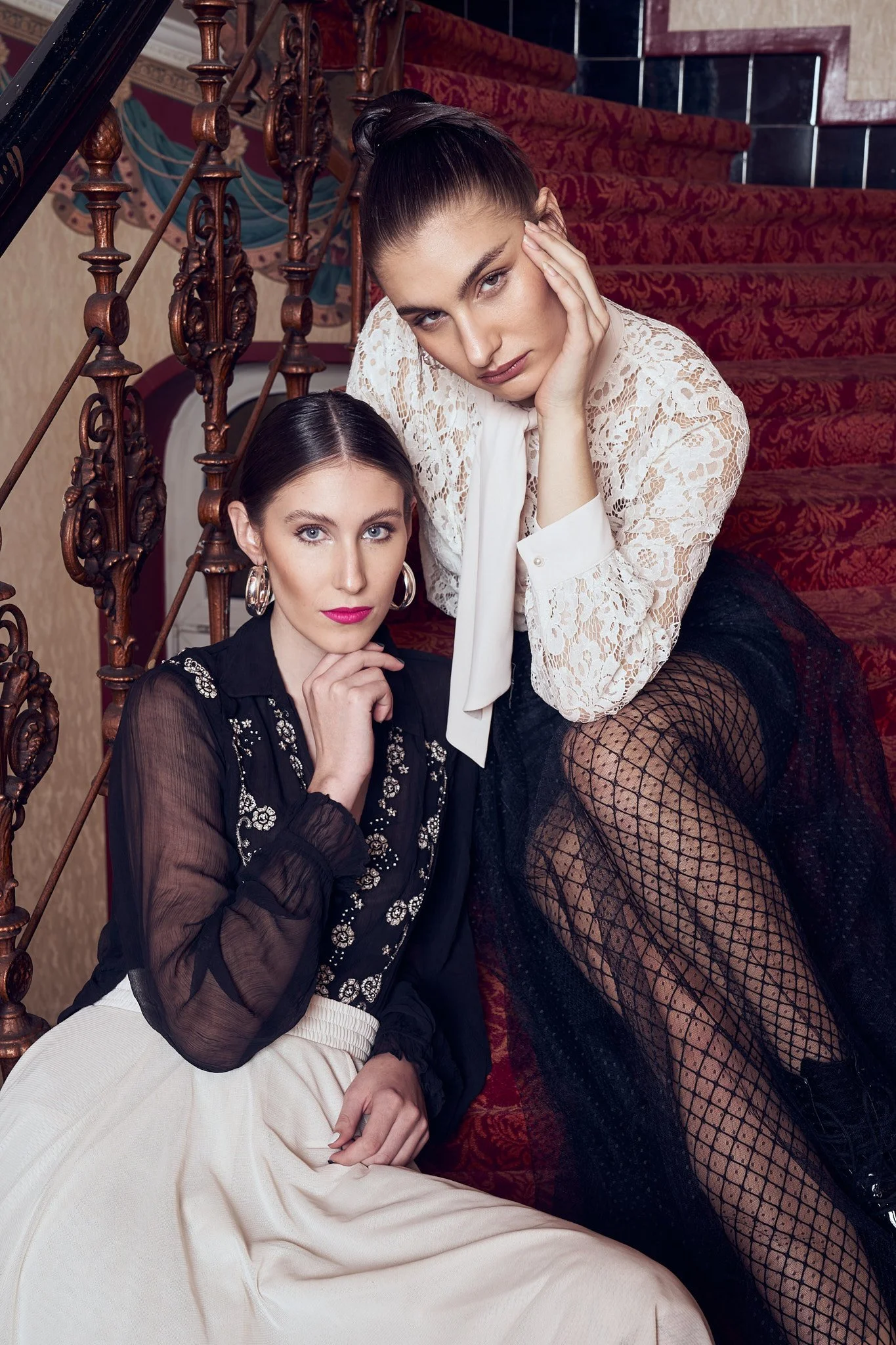 Duo mode sur un escalier rouge, entre dentelle noire et blouse victorienne. Photographie éditoriale belge.