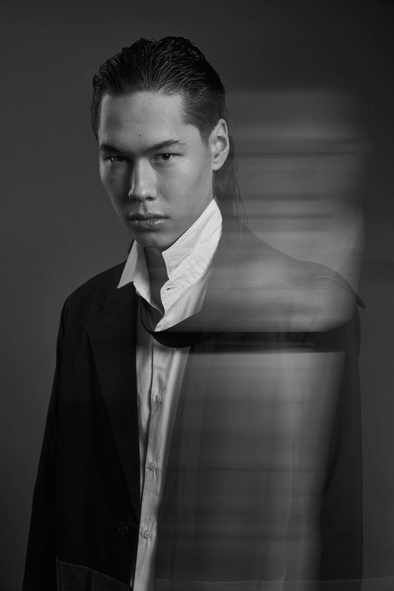 Black and white menswear editorial portrait photographed by Belgian fashion photographer Simon Rogghe in Ghent. The male model wears a classic white shirt and tailored black blazer, enhanced by subtle motion blur that creates a surreal, cinematic eff