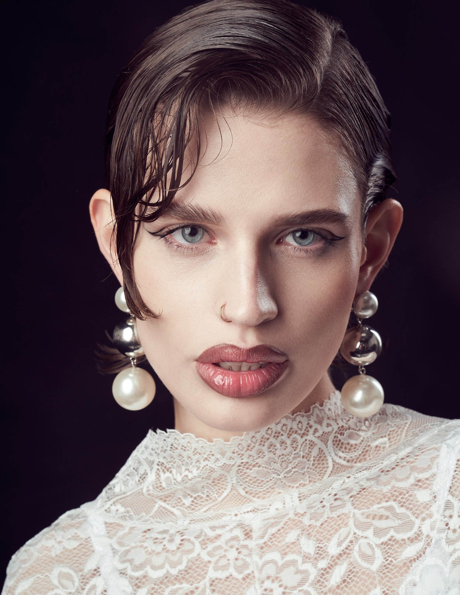 Close-up beauty portrait of a dark-haired model wearing multi-drop pearl earrings and a high-neck white lace top.⁠