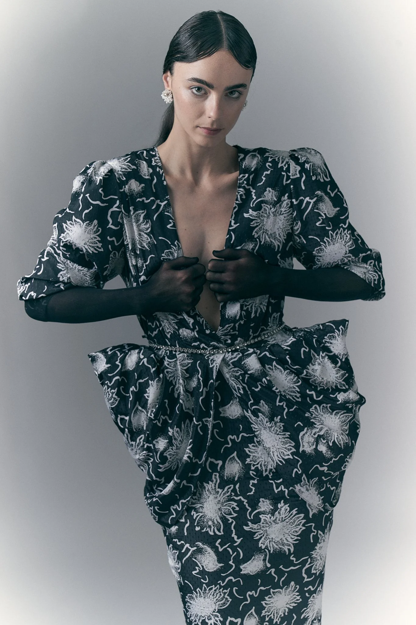 Three-quarter studio portrait of a model wearing a deep V-neck black-and-white jacquard pattern dress with sheer black sleeves.⁠
