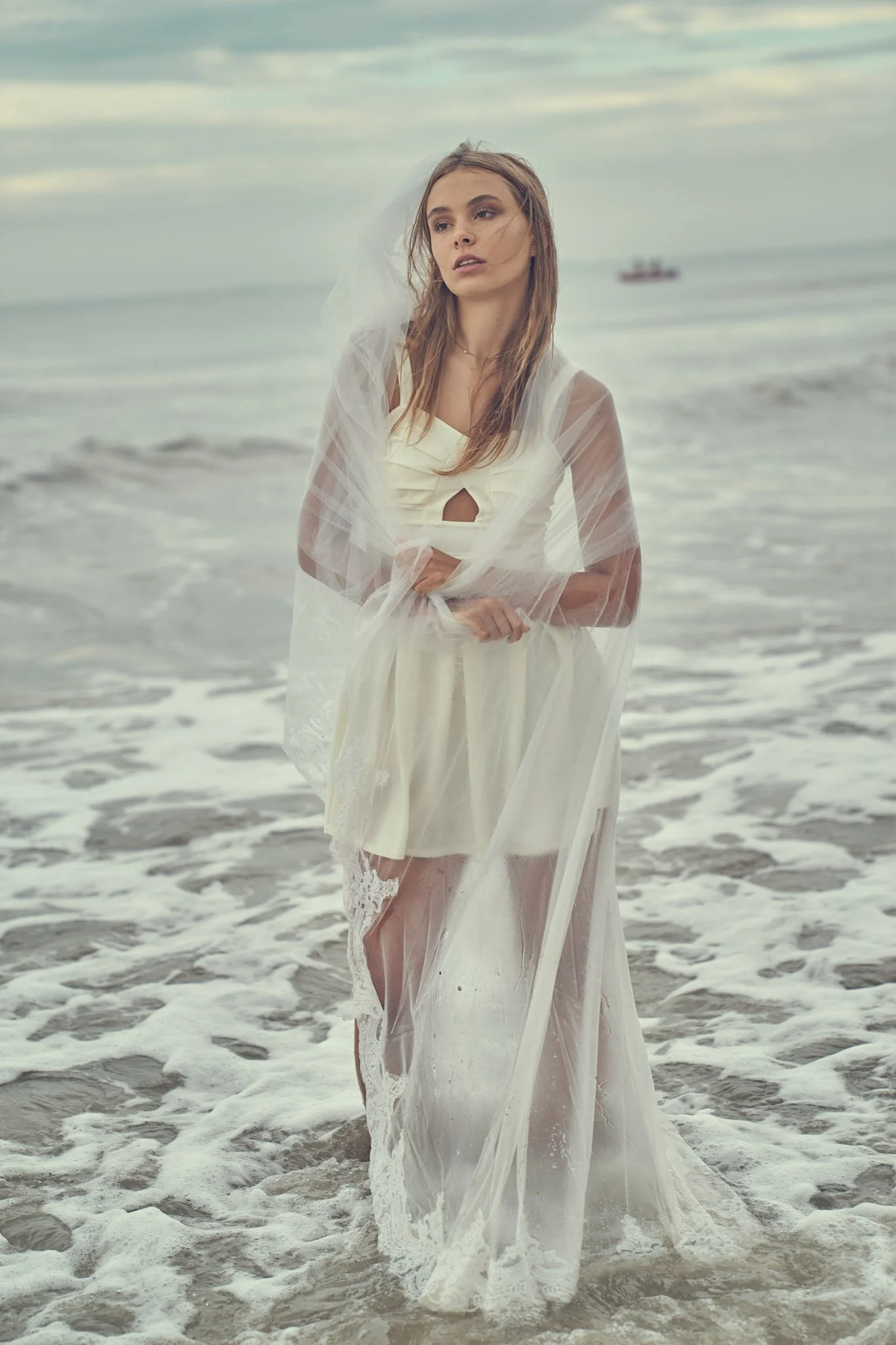 Ethereal seaside editorial with bridal styling. Shot in Belgium with soft waves and overcast skies.