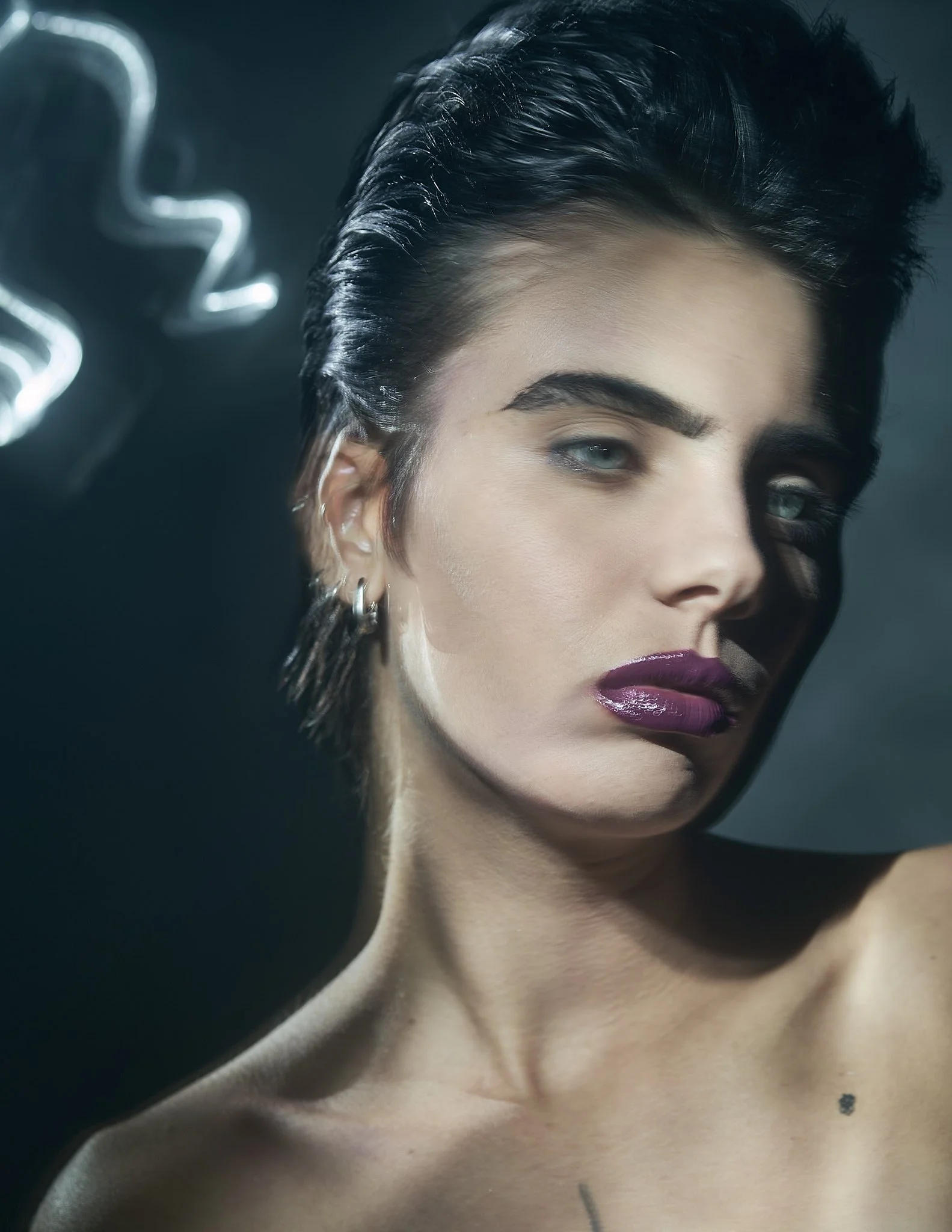 Close-up editorial portrait of a model with slicked-back dark hair, striking dark purple lipstick, and soft light trails in the background.⁠