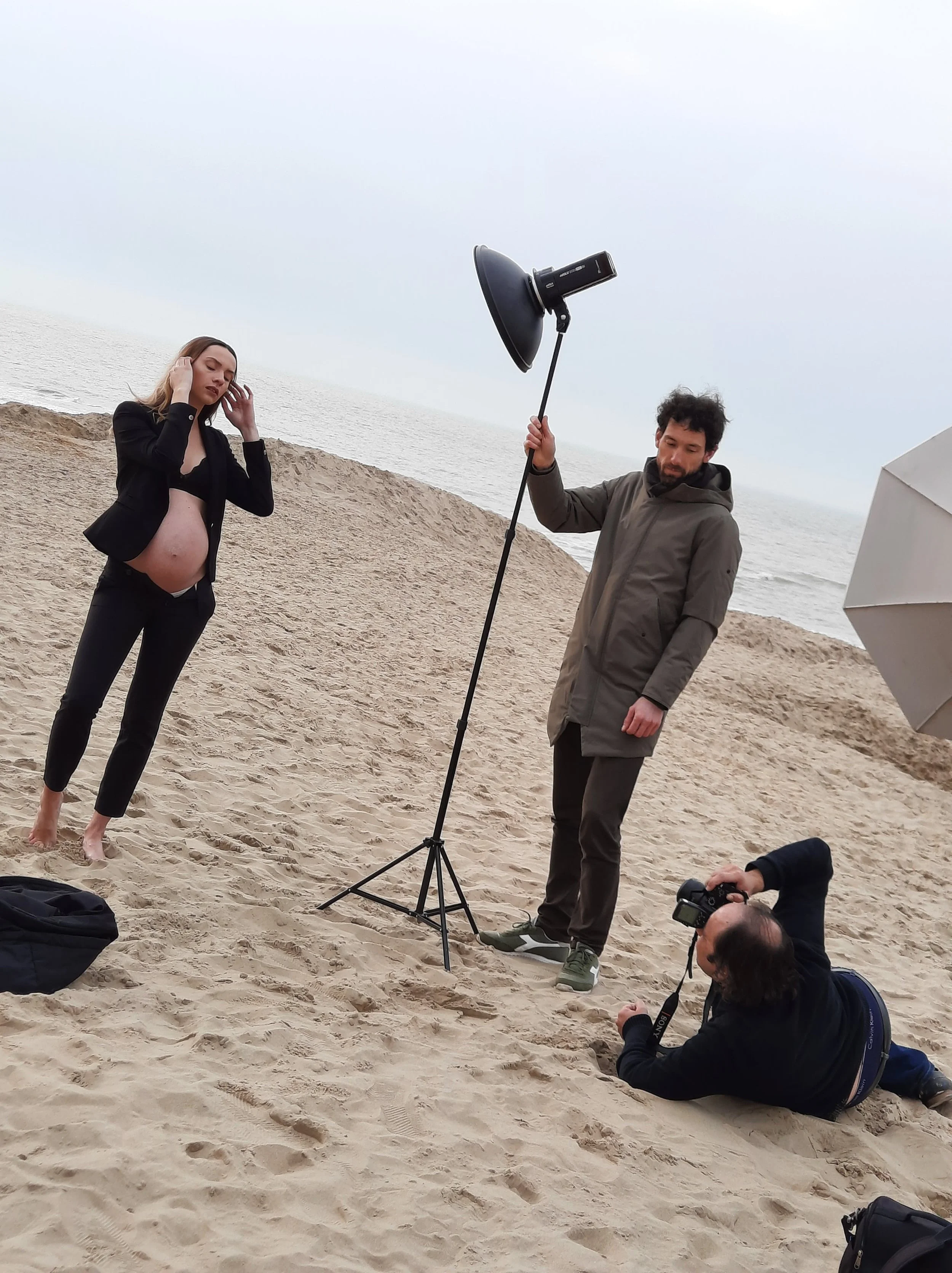 Achter de schermen bij een professionele zwangerschapsshoot op het strand – fotograaf en lichtopstelling in actie.