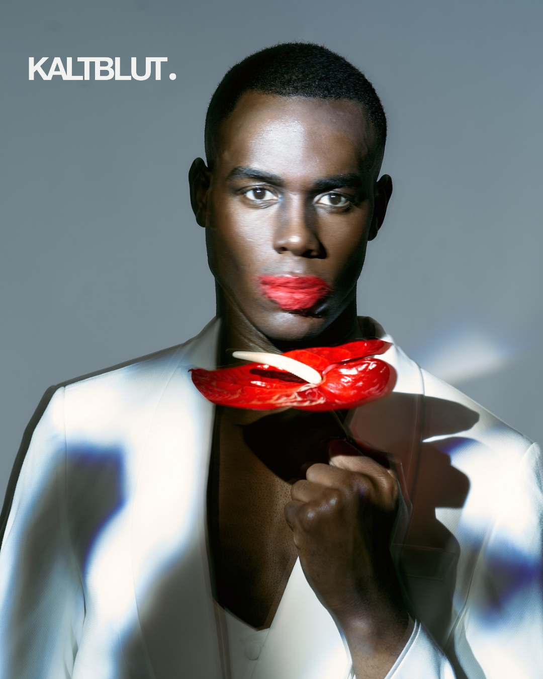 Fashion portrait of Black male model wearing white blazer and bold red lips holding red flowers, high-contrast editorial lighting, contemporary fashion photography