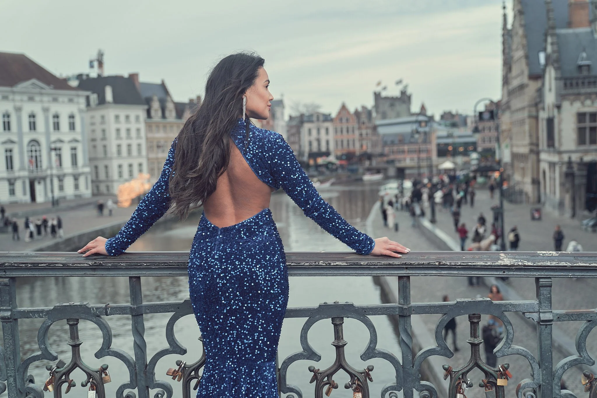 Glamorous back view of a woman in a sequined gown posing on Graslei bridge in Ghent, Belgium — luxury portrait session in iconic Flemish architecture setting.