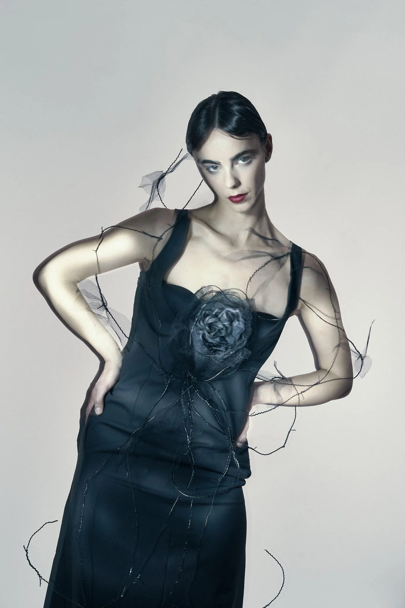 Studio fashion portrait of a model wearing a black structured corset dress featuring delicate botanical wire accents.⁠