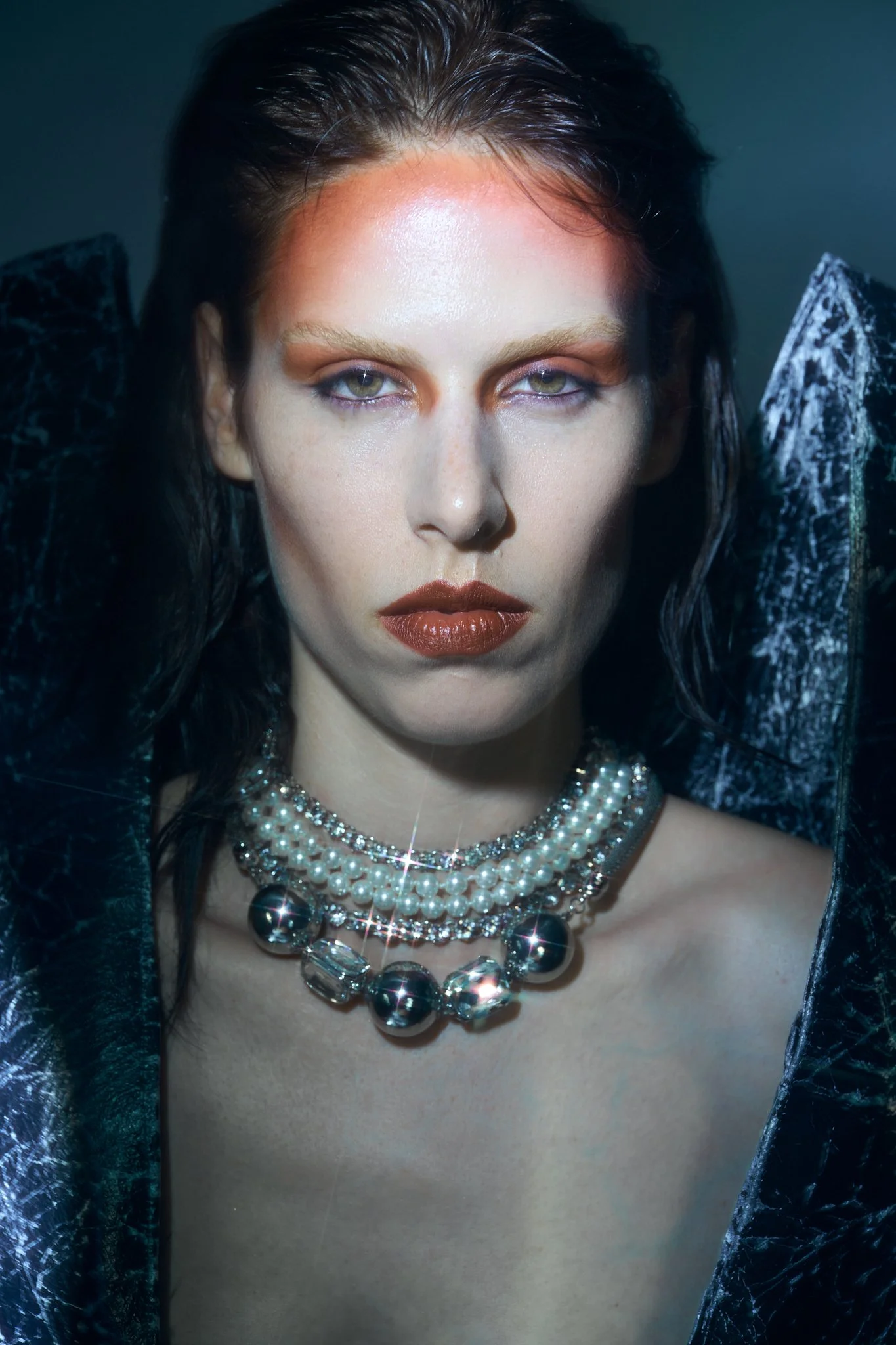 Close-up beauty portrait of a fashion model wearing dramatic editorial makeup, layered pearl and crystal jewelry, and an avant-garde black garment, photographed by a Belgian fashion photographer.