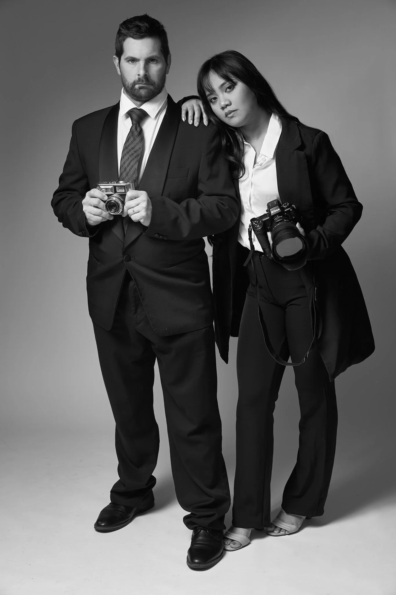 Zwart-wit bedrijfsportret van twee fotografen in elegante zakelijke kledij, gemaakt in een studio in Gent, Oost-Vlaanderen. Professionele brandingfoto die kracht en samenwerking uitstraalt, gefotografeerd door Simon Rogghe Photography