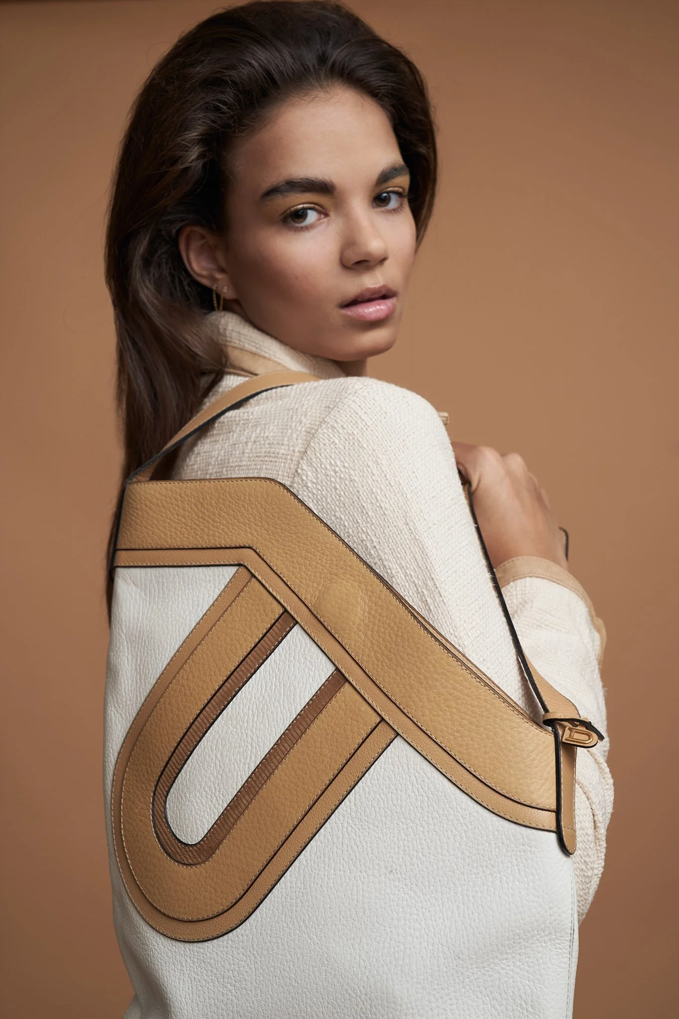 Close-up beauty and fashion portrait of a female model carrying a structured designer bag, shot on a beige backdrop — clean, high-end model portfolio photography in Ghent.
