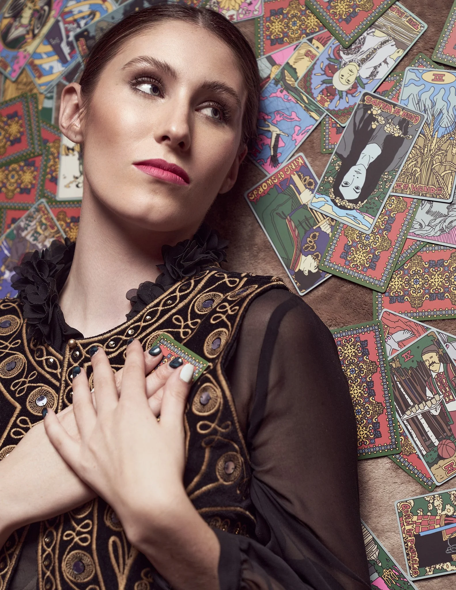 Close-up fashion portrait of a model in an embellished high-neck blouse with tarot cards arranged in the background.⁠