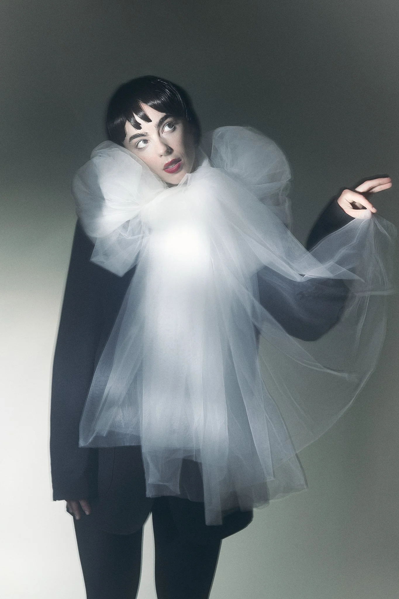 Half-length portrait of a model wearing a dramatic, voluminous white tulle neck ruffle over a dark oversized tailored blazer.⁠