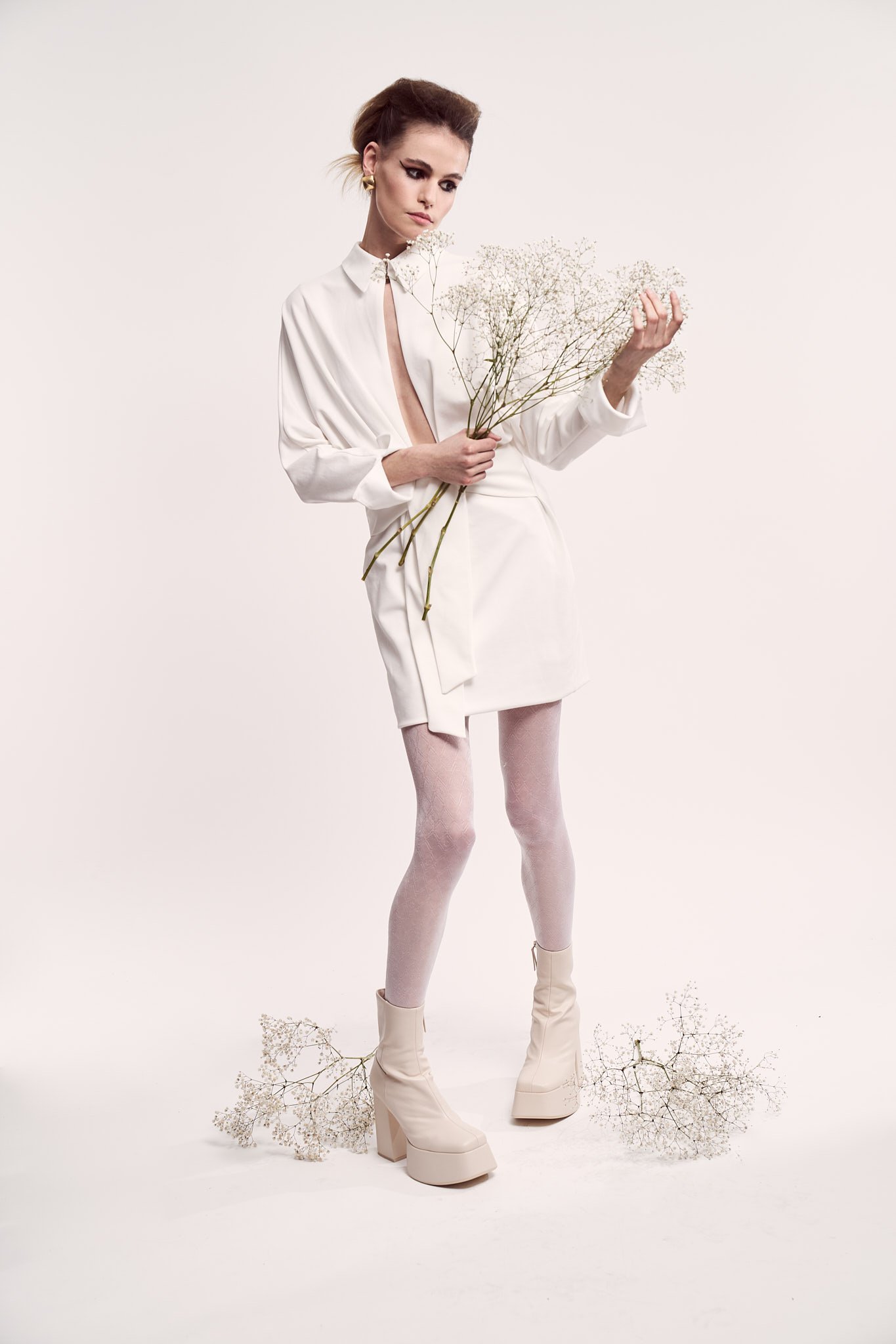 Studio portrait of a model wearing a sleek white collared dress shirt, holding a bouquet of delicate white baby's breath flowers.⁠