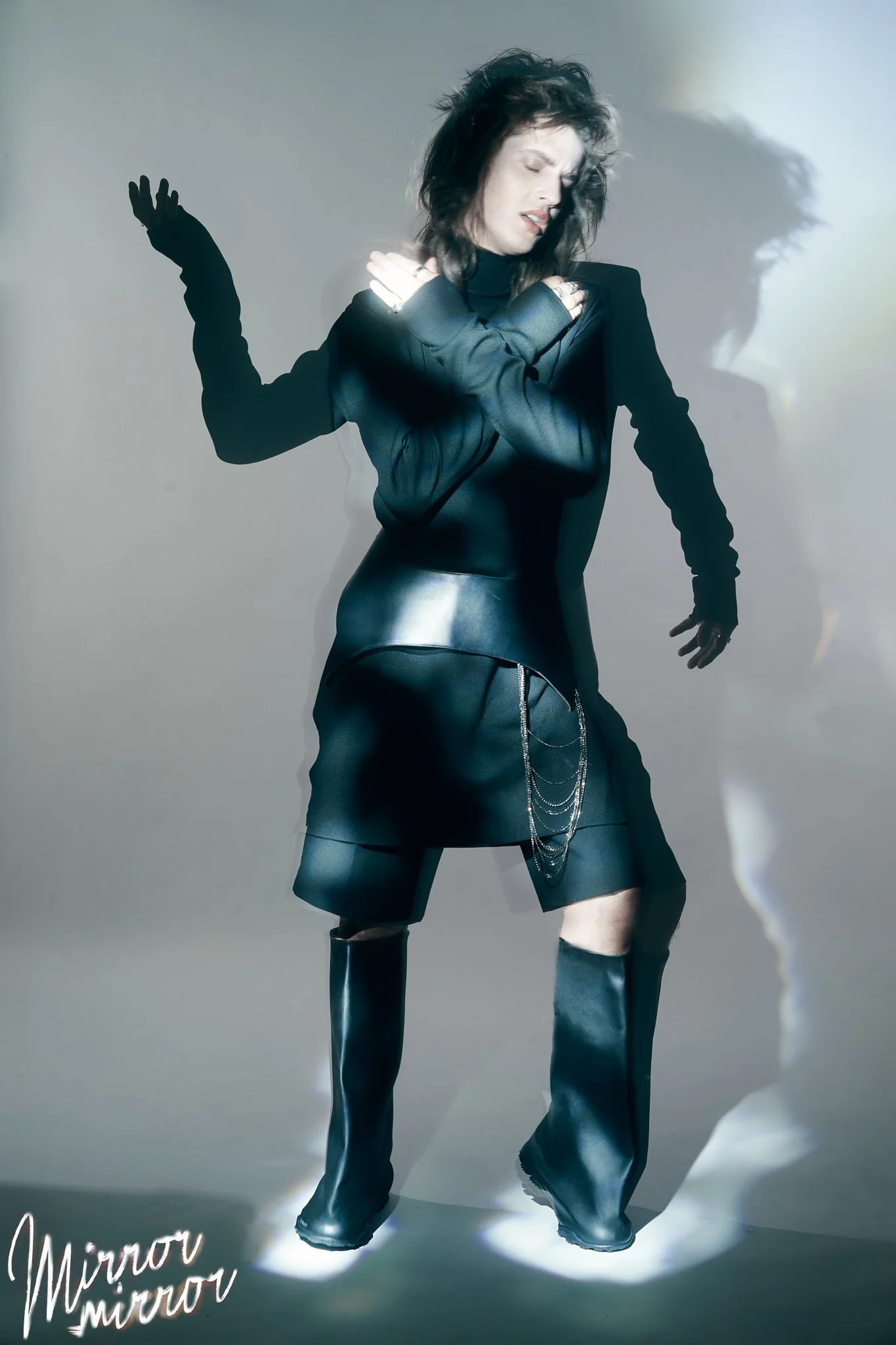 Editorial fashion portrait of model in black Rick Owens turtleneck and corset belt by THE MUSE, wearing Rombaut boots, with sculptural lighting and shadow play, photographed in studio