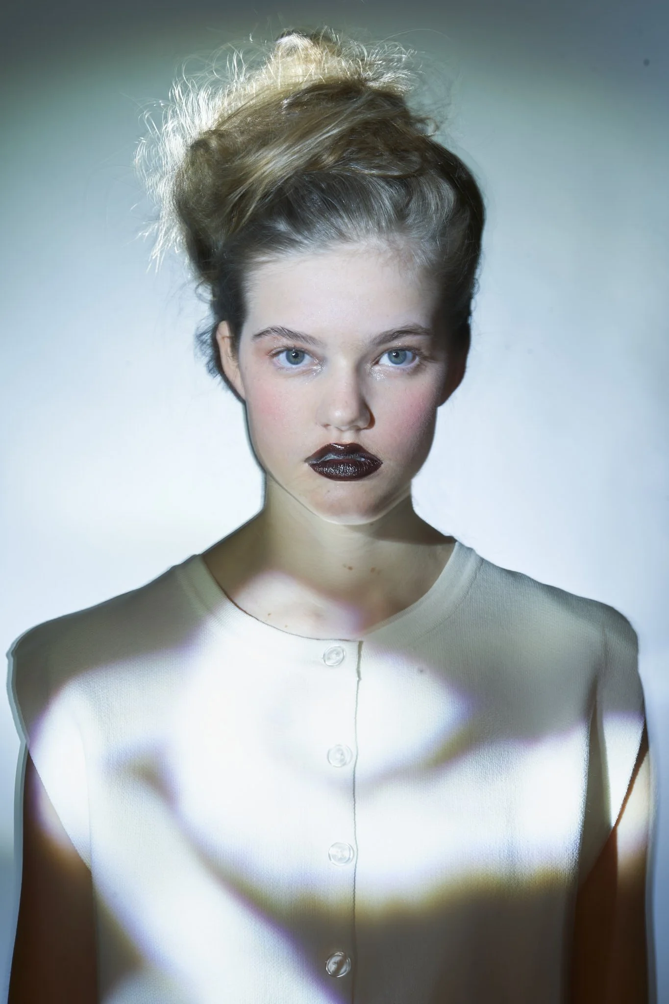 Avant-garde beauty portrait of a young model with sculptural updo and dark glossy lips, photographed with ethereal light patterns by Belgian fashion photographer in Ghent.