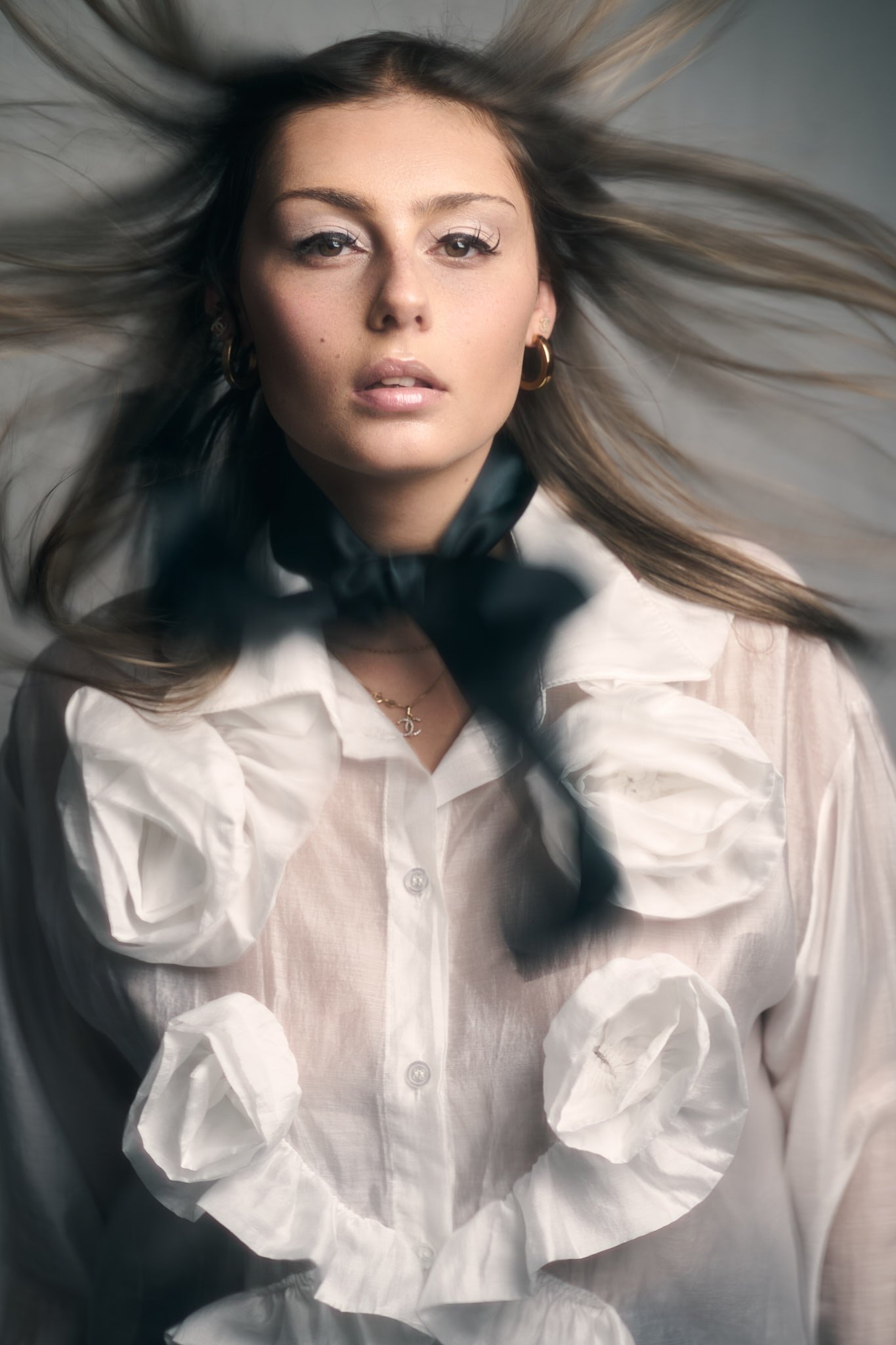 Editorial fashion portrait of a woman in a white sculptural blouse with wind-blown hair, captured in a fine art aesthetic by Belgian photographer Simon Rogghe.