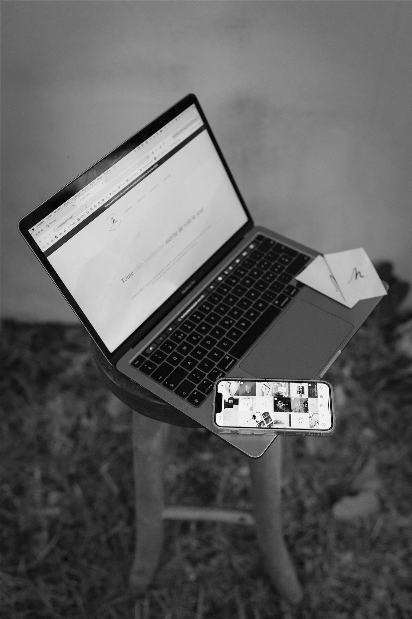 Un ordinateur portable posé sur une petite table, avec un téléphone portable à côté. La table est en bois, et l'image est en noir et blanc.