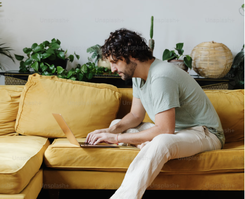 A man with dark curly hair and a beard using a pink laptop on a yellow sofa. Accelerated healing for adults who want fast results—not just talk. In-person therapy in Philadelphia & online throughout PA, NY, NJ, & FL.