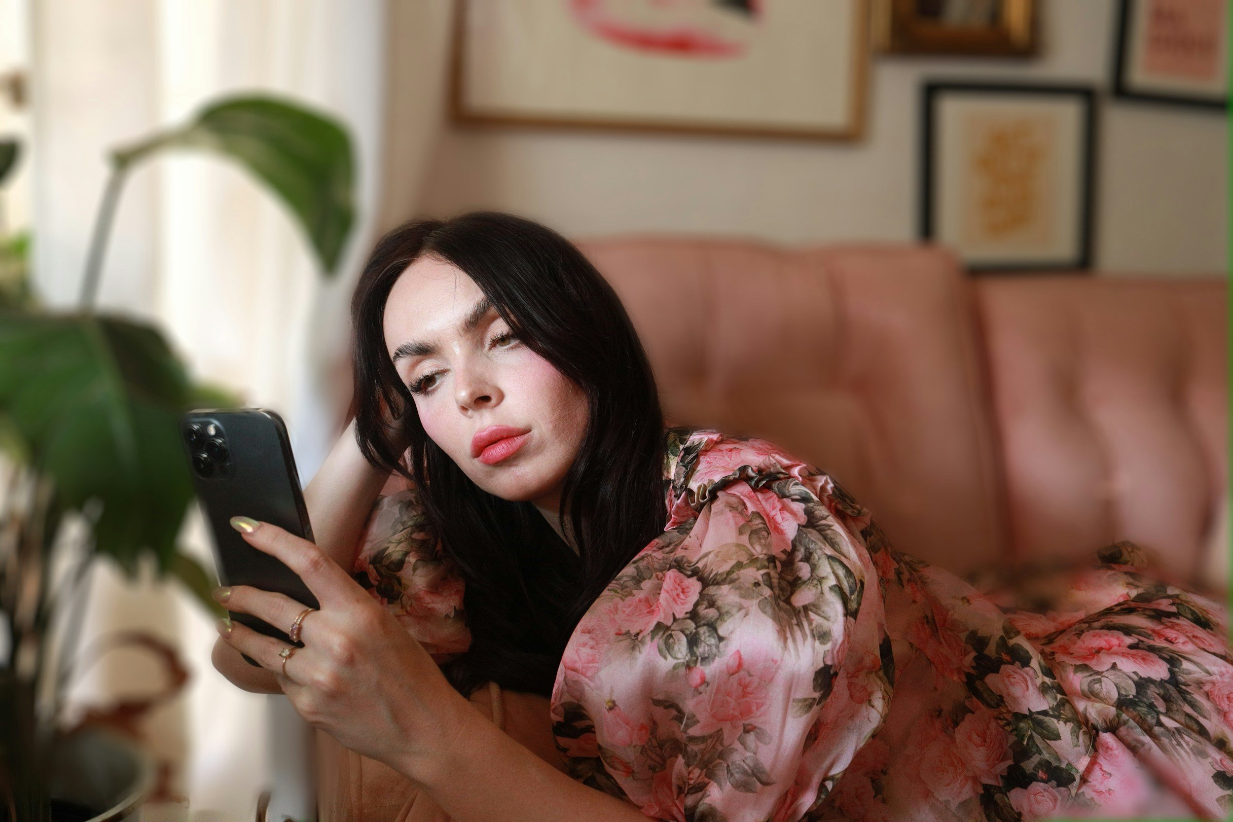 A woman with dark hair and wearing a floral robe lies on a pink couch, looking at her smartphone with a neutral expression. Accelerated healing for adults who want fast results—not just talk. In-person therapy in Philadelphia & online throughout PA,