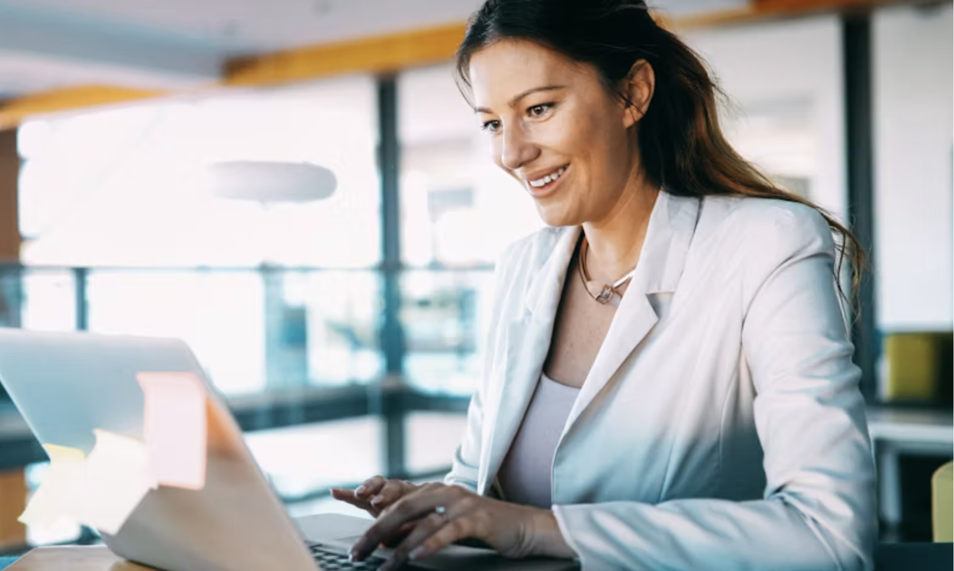 A woman working on a laptop in a bright office space, smiling, wearing a light blazer and necklace. Accelerated healing for adults who want fast results—not just talk. In-person therapy in Philadelphia & online throughout PA, NY, NJ, & FL.