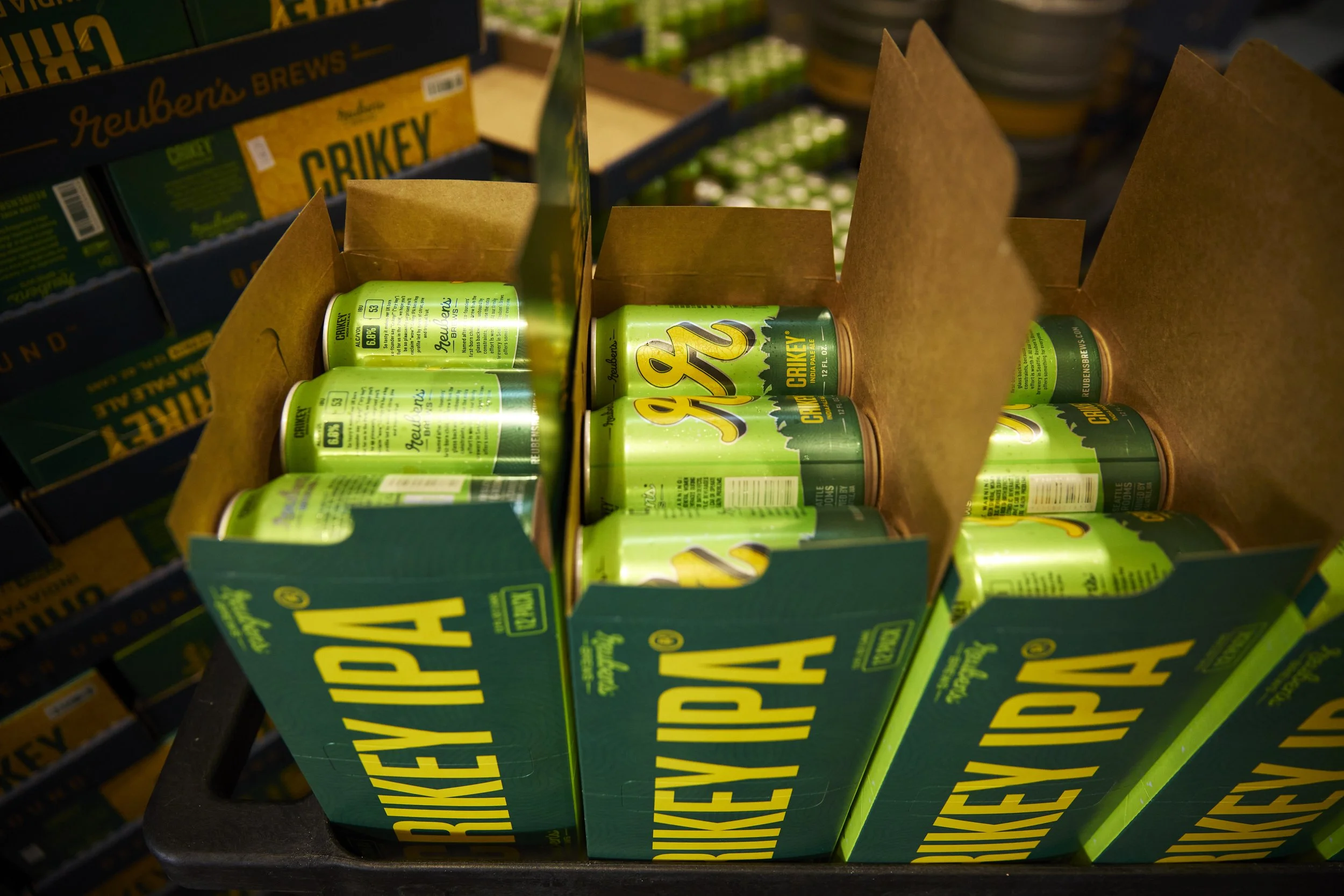 Green cans of Reuben's Crikey beer in a cardboard display box on a store shelf.