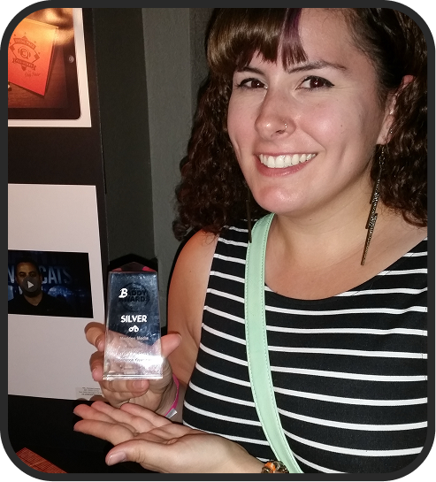 Woman smiling and holding a glass award with 'Silver' written on it, wearing a black and white striped top and earrings.