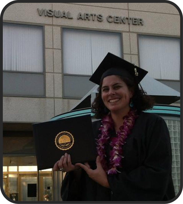 A woman in a graduation cap and gown holding a diploma, standing in front of the Visual Arts Center building.