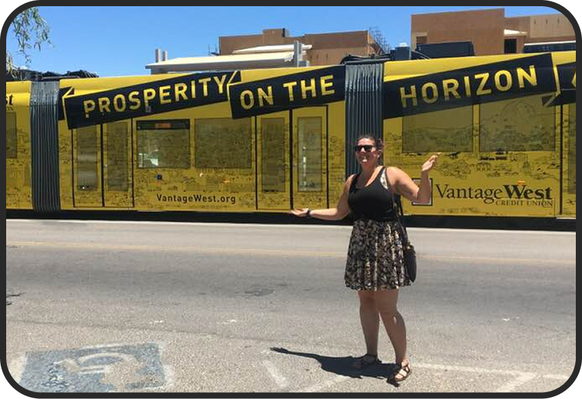 A woman standing on a street in front of a yellow and black display with a message 'Prosperity on the Horizon' promoting Vantage West Credit Union.