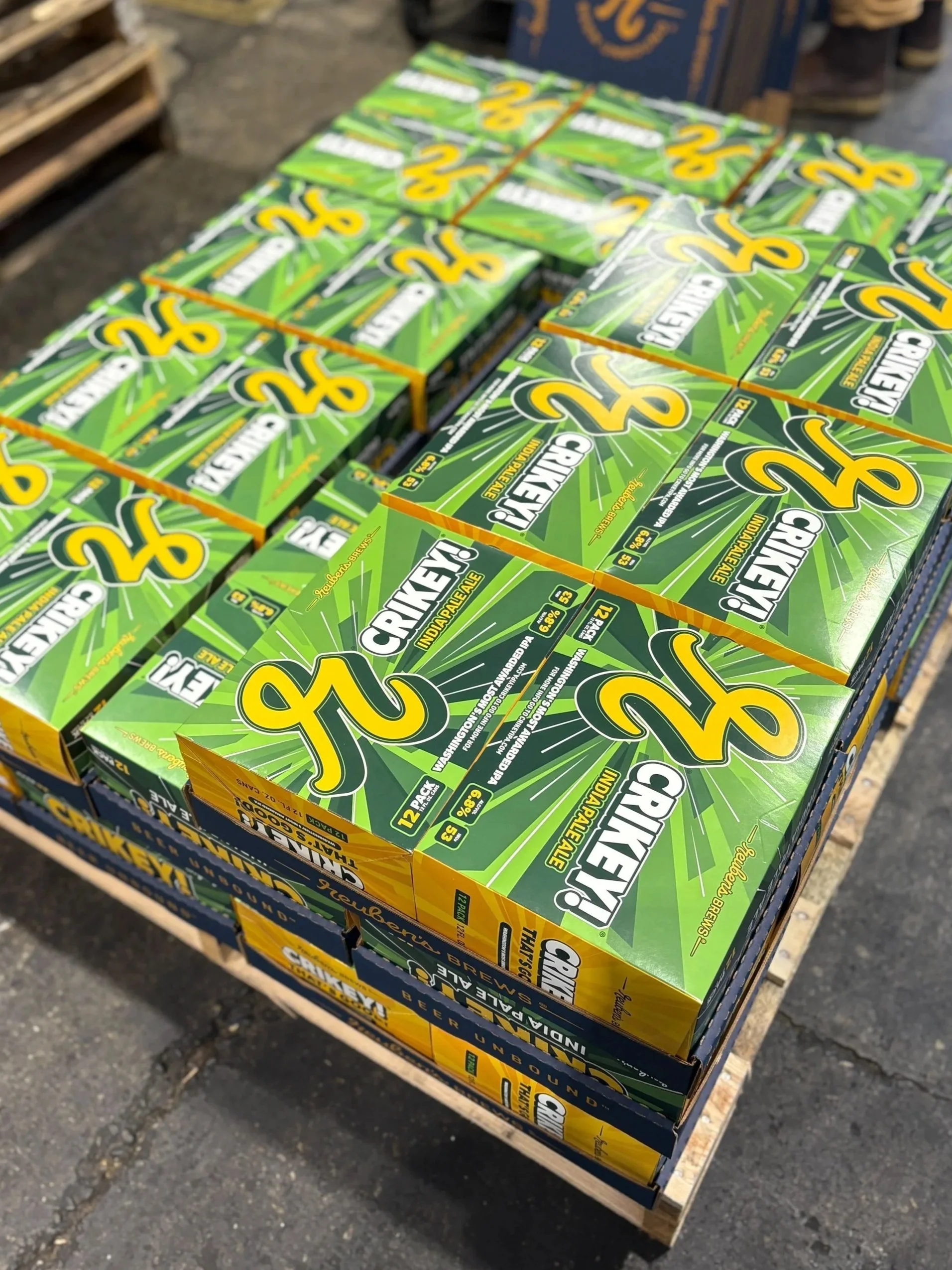 Multiple boxes of Crikey! Indiana Pale Ale beer stacked on a wooden cart at a store or market.