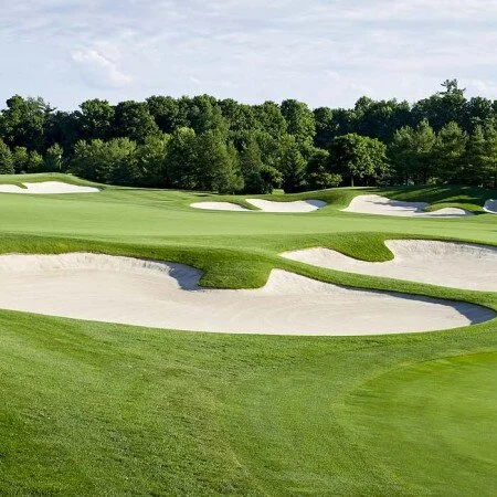 A golf course with sand bunkers, green fairways, and trees in the background.