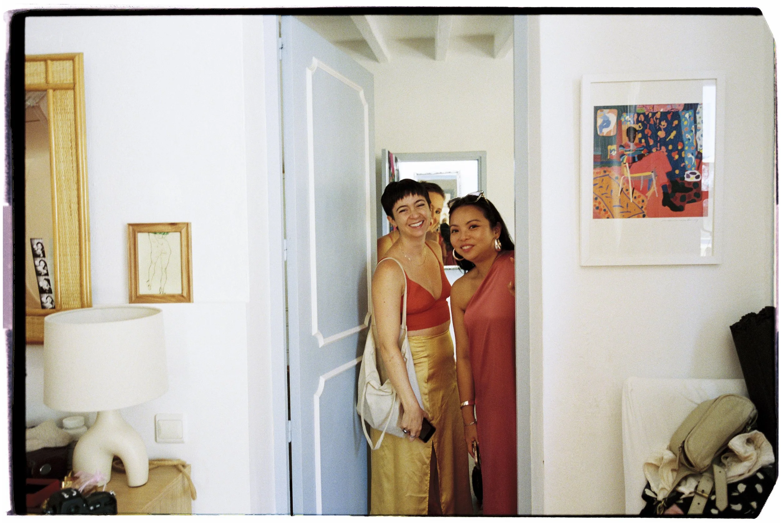 Two women standing in a doorway, smiling, in a bright room with wall art and furniture.