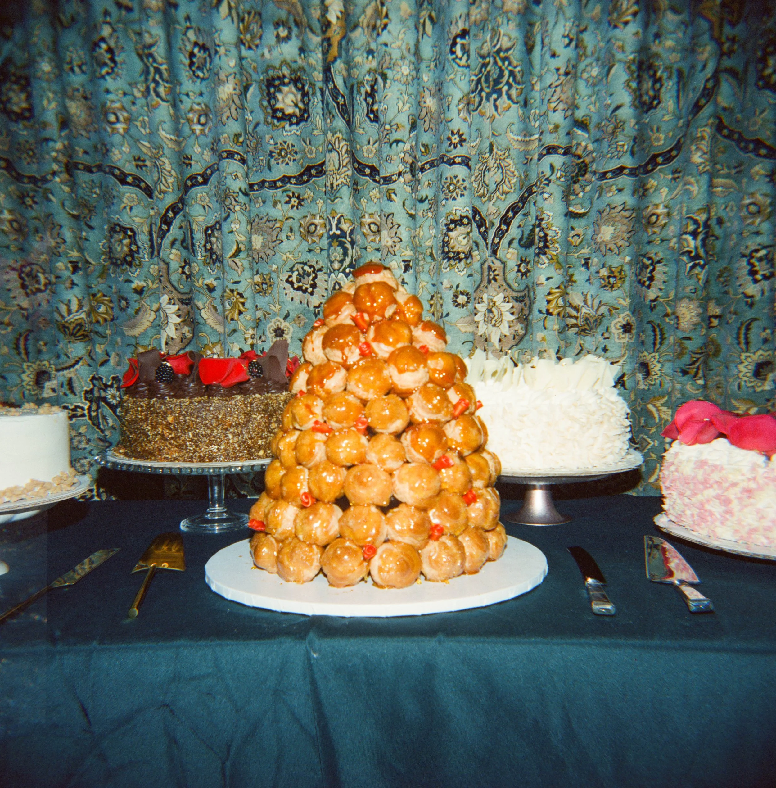 Dessert table with croquembouche and various cakes in front of a patterned curtain.