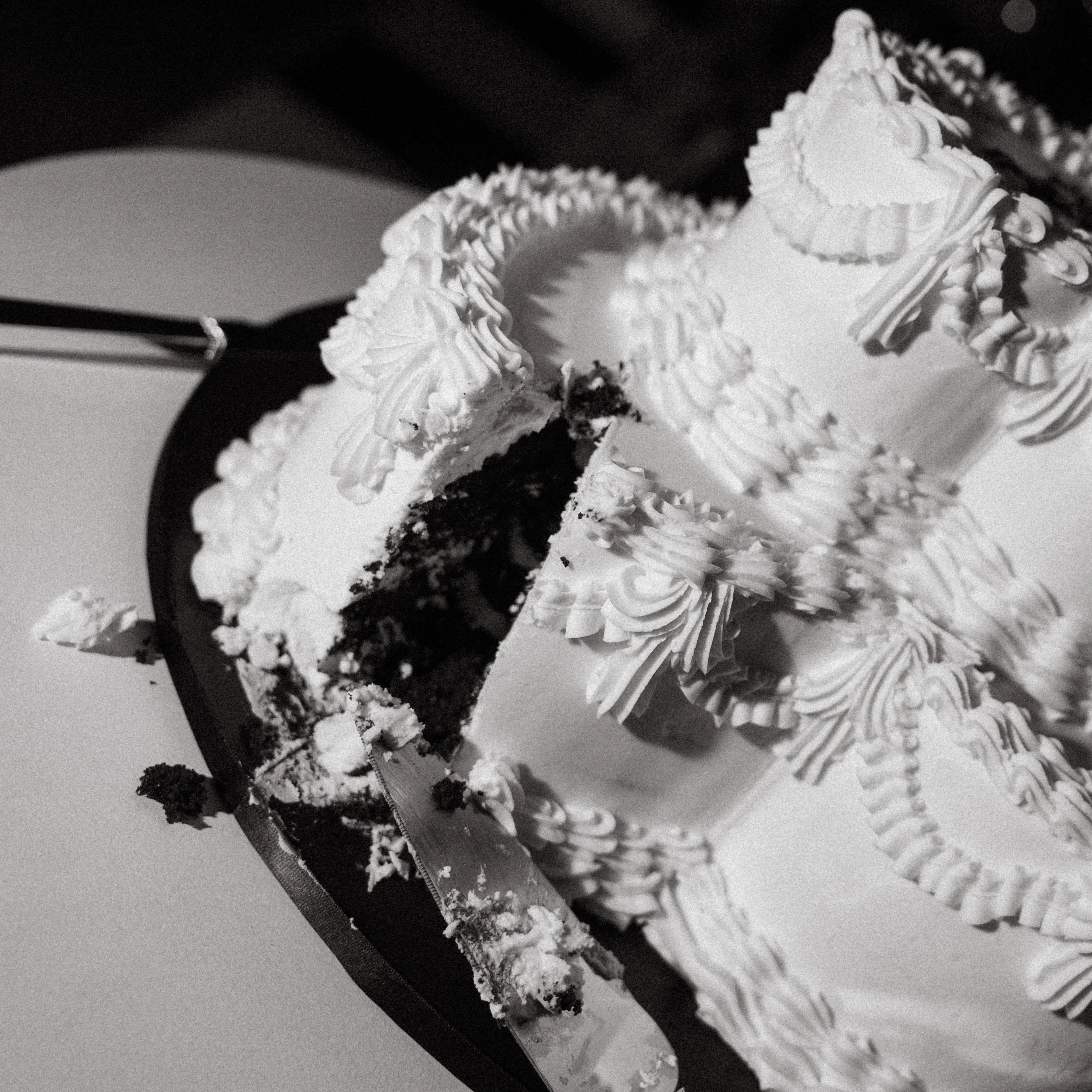 A partially eaten layered cake with white frosting and decorative piping on top, on a round cake board with a cake server nearby.