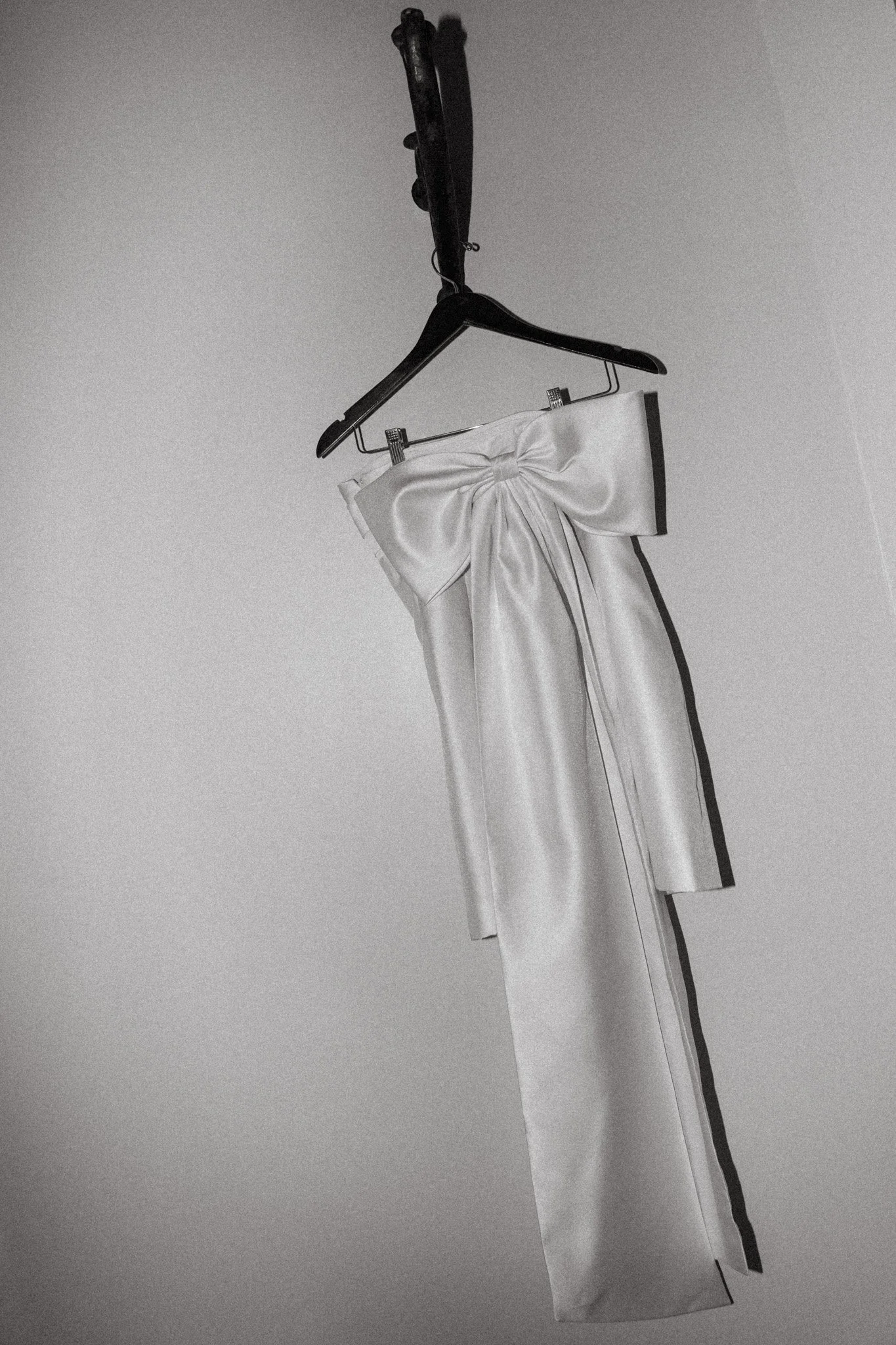 A white jumpsuit with a large bow on the bodice, hanging on a black hanger against a plain wall.
