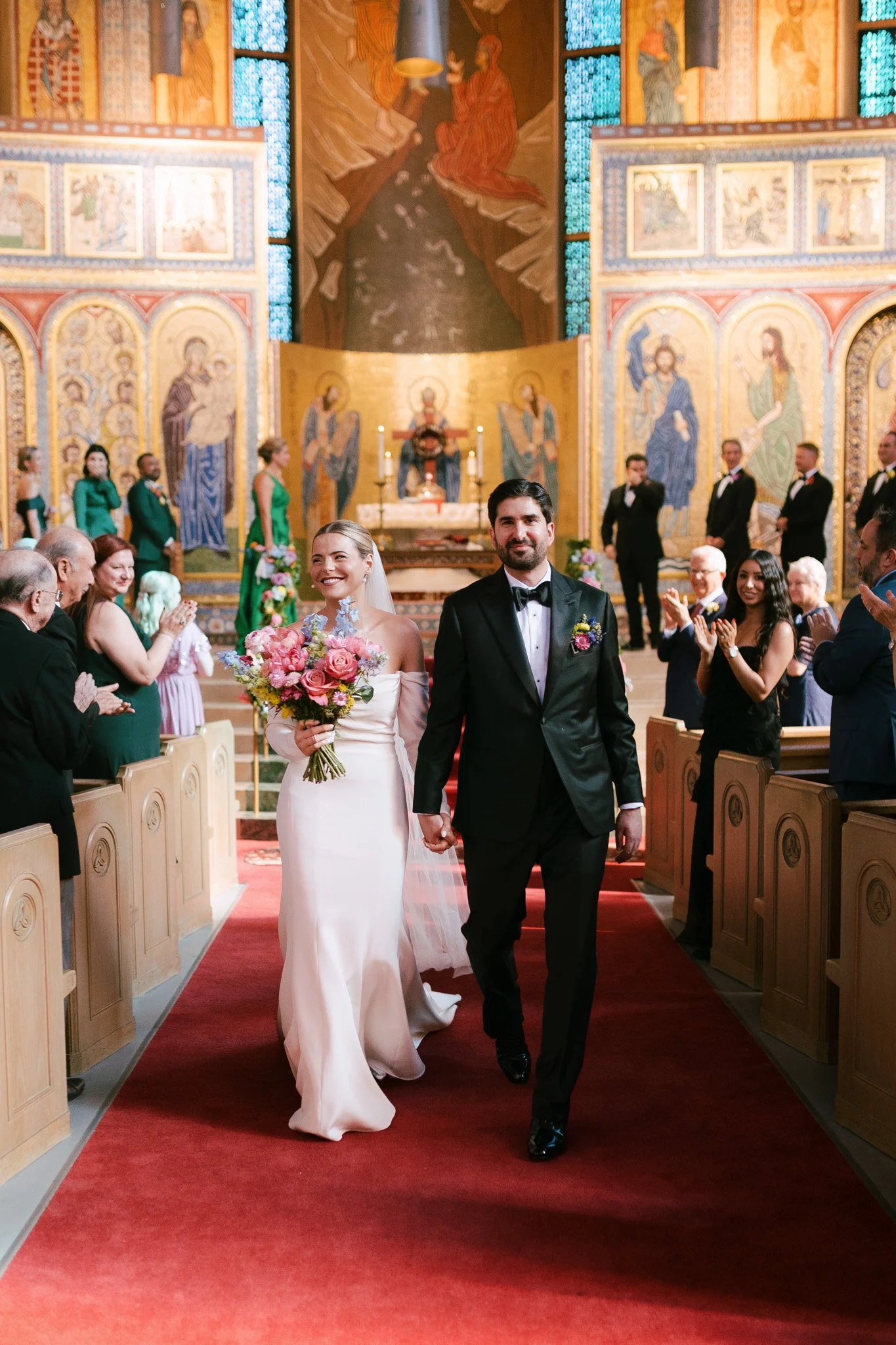 A bride and groom holding hands, walking down the aisle of a church after their wedding ceremony, surrounded by smiling guests.