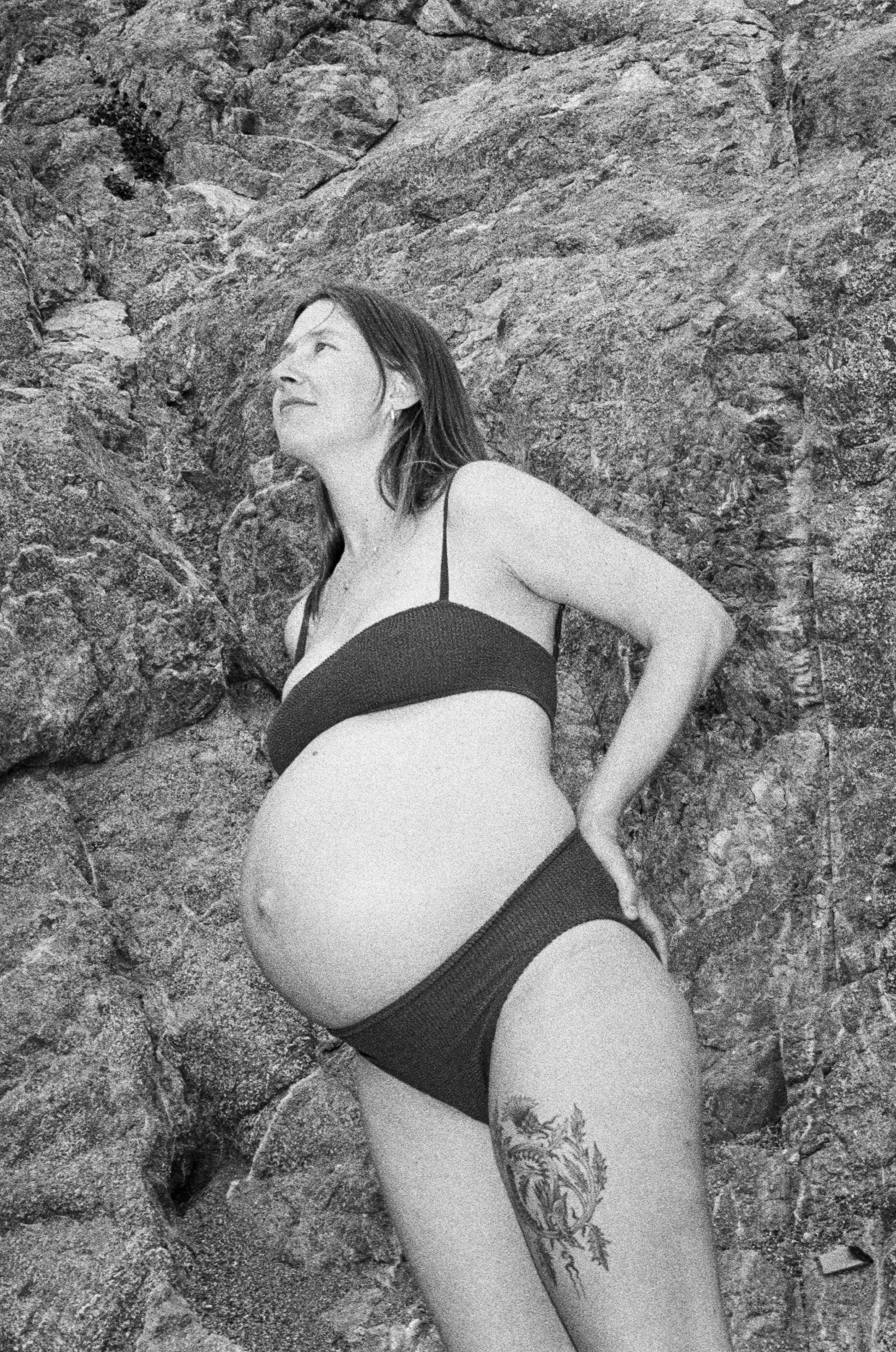 A pregnant woman in a bikini standing against rocks.