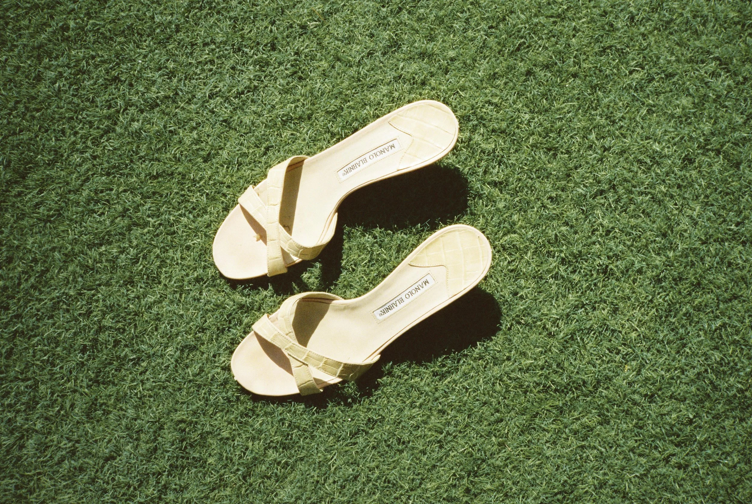 Pair of beige high-heeled sandals on green grass, with the brand 'MALOU BALIK' visible inside the shoes.