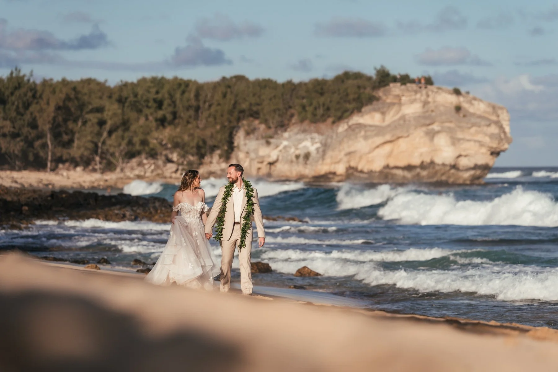 Bride and groom in a ti leaf lei walking hand in hand on Shipwreck Beach beside the Grand Hyatt Kauai in Poipu