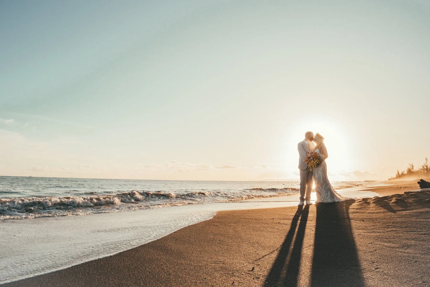 Bride and groom embrace at sunset on black sand beach at Waimea Plantation Cottages, Kauai